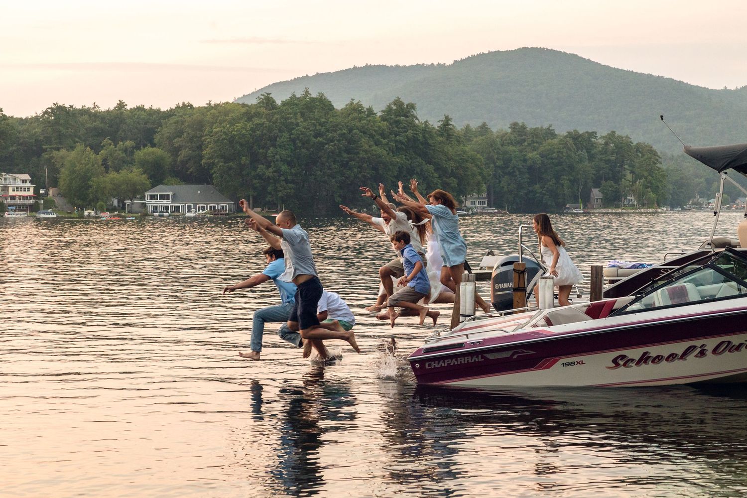 Scenic lake view with boats and water sports activities at sunset with mountains in background.