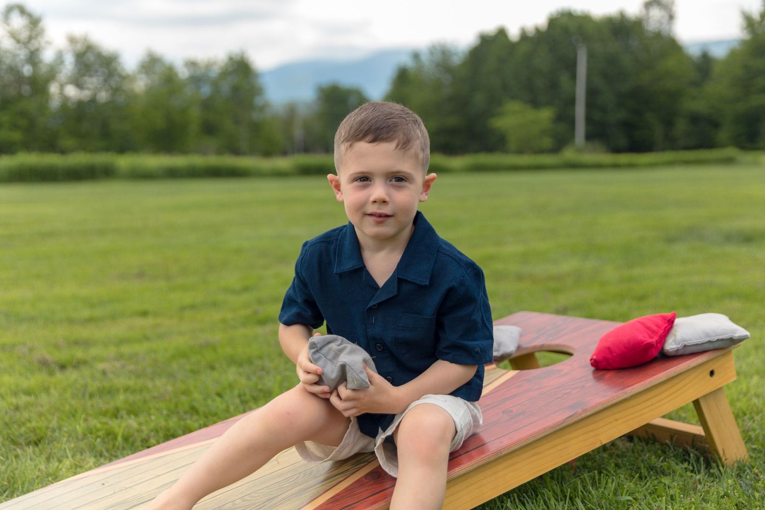 Child playing on wooden cornhole board in an outdoor setting.