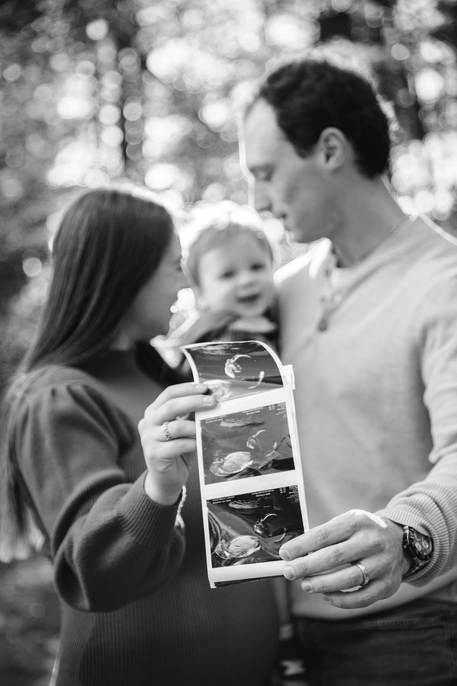 Black and white photo showing hands holding ultrasound photos in a natural outdoor setting.