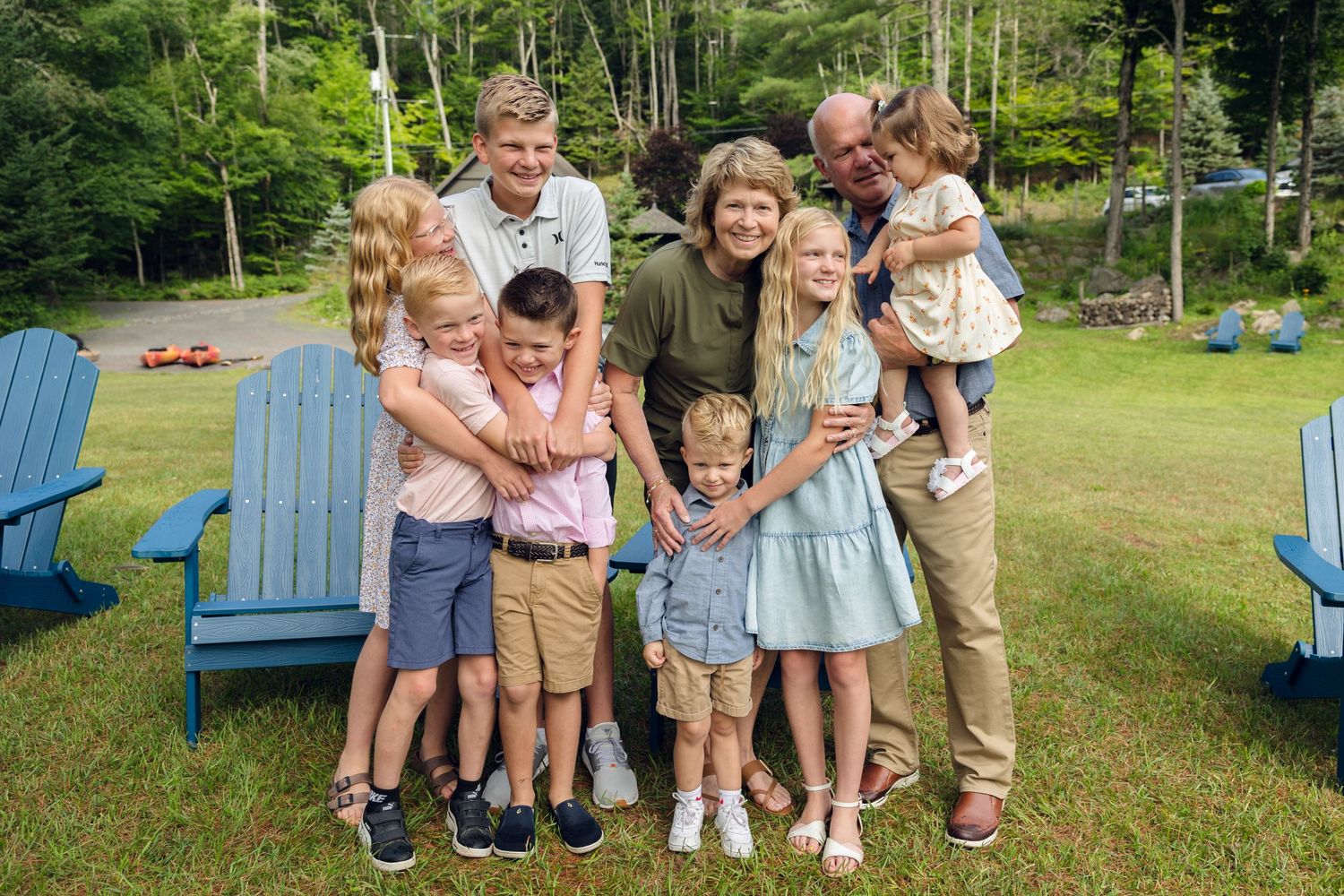 Large family group poses together on lawn with blue Adirondack chairs in background.
