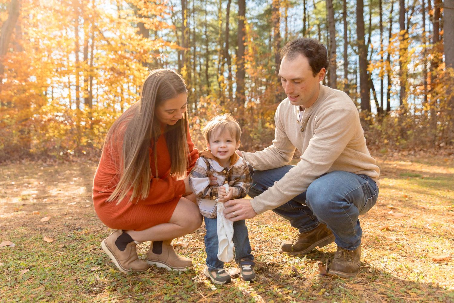 A family plays together on fallen leaves during a sunny autumn day in the woods.