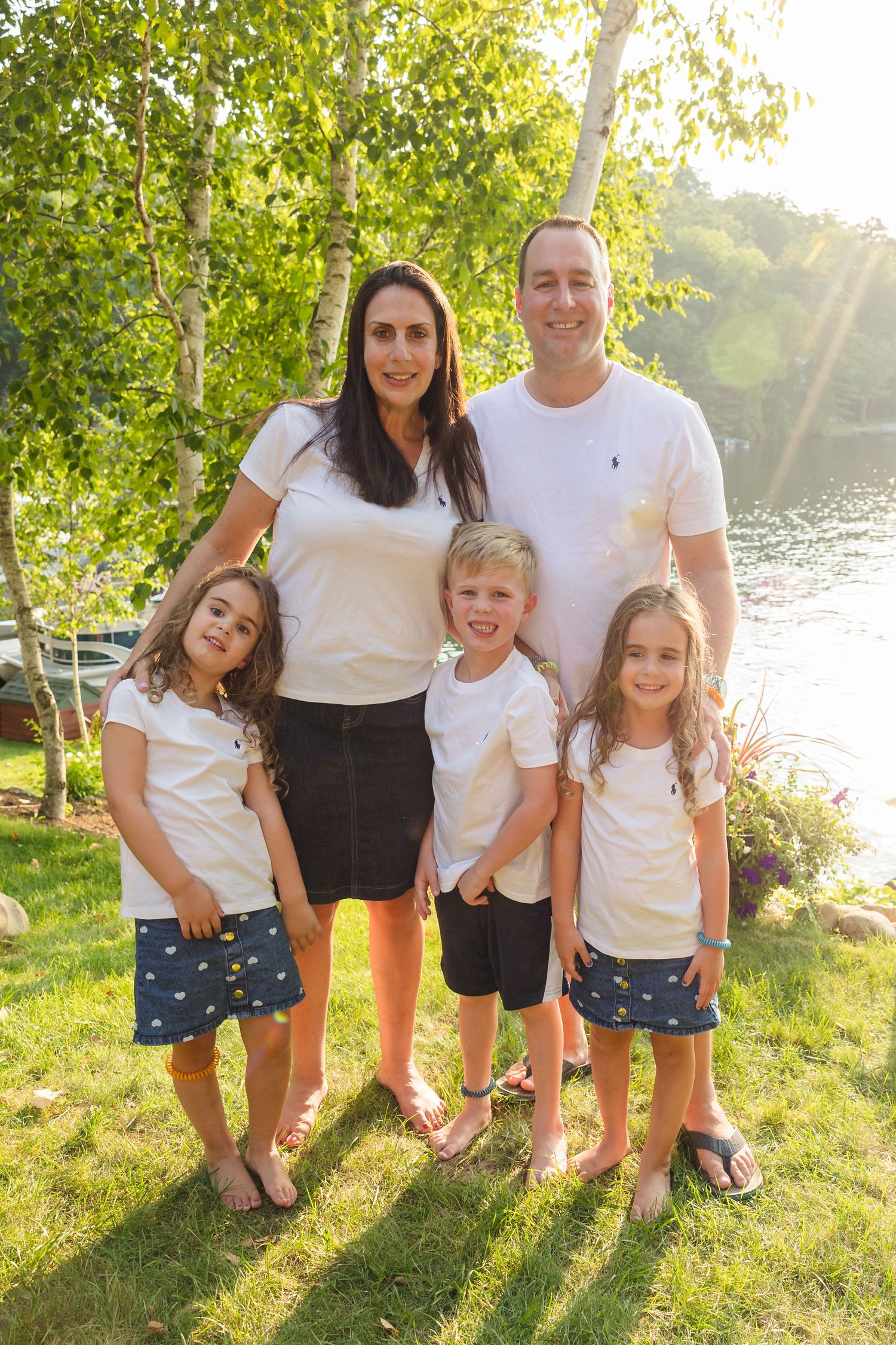 Family wearing coordinated white shirts and polka dot shorts poses together by a lake at sunset.