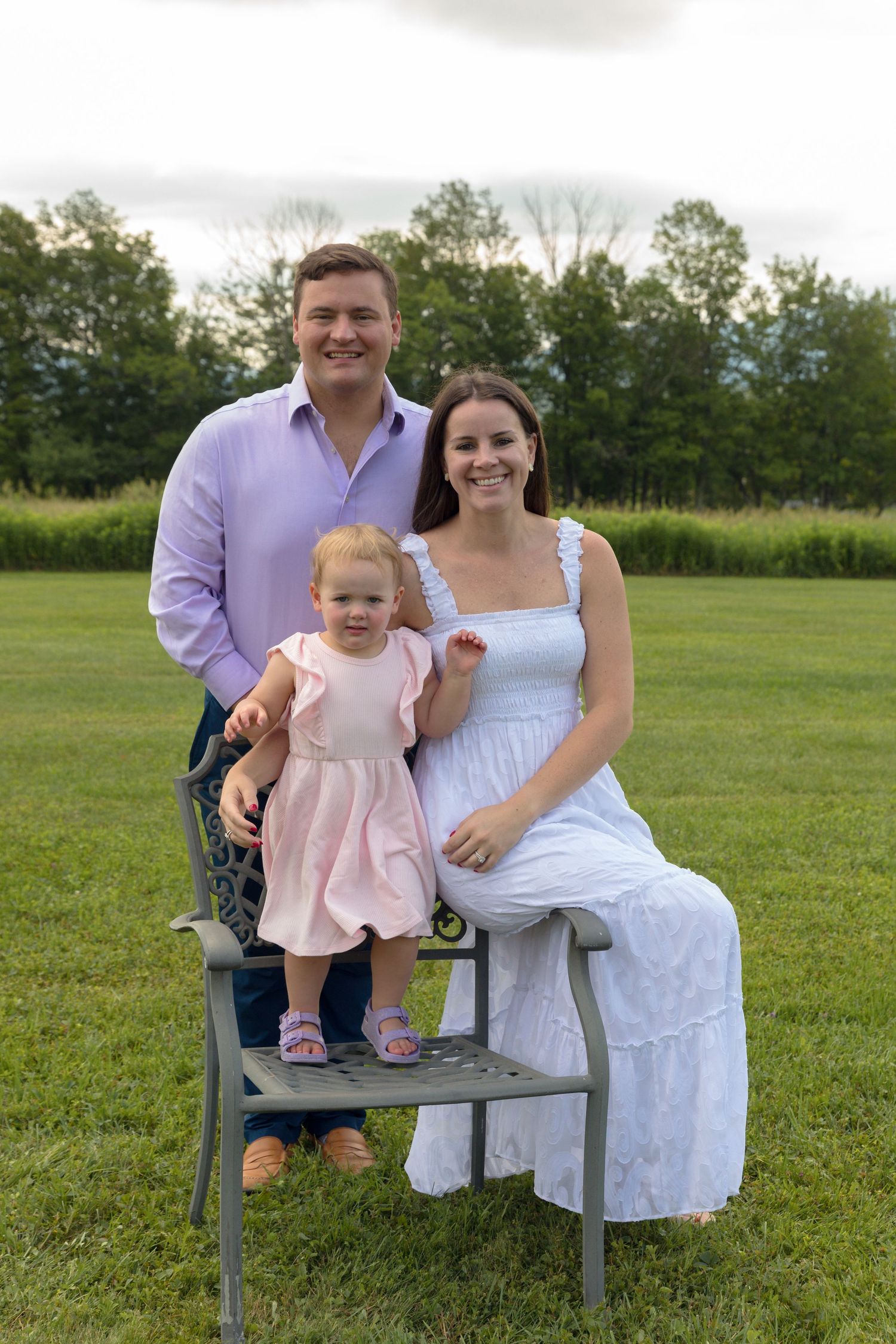 Family portrait on a grey bench in a serene meadow setting.