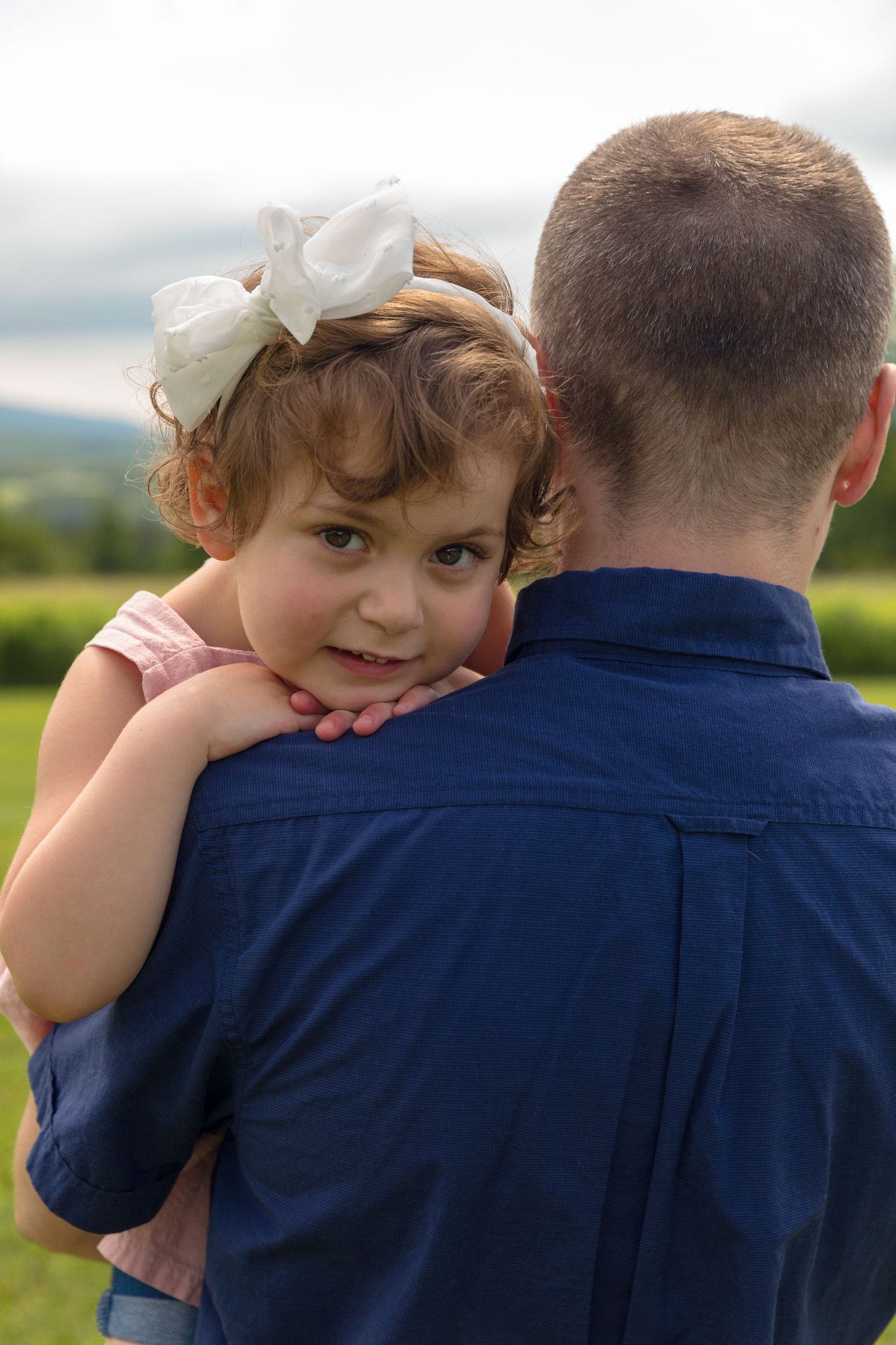 Sweet candid moment captured of a young child in white being held against navy blue shirt.