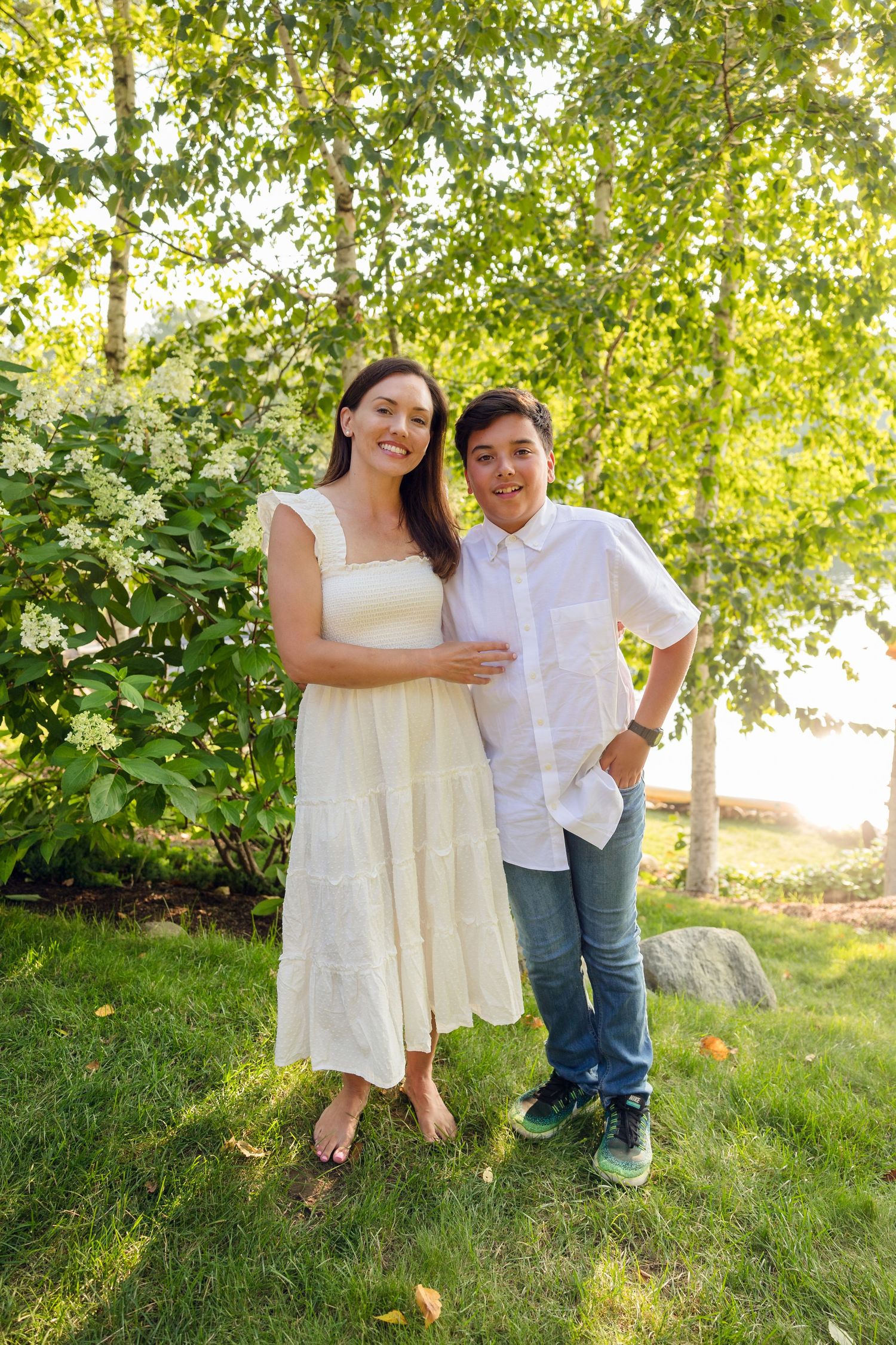 Couple in white and casual attire poses together on grass under birch trees.