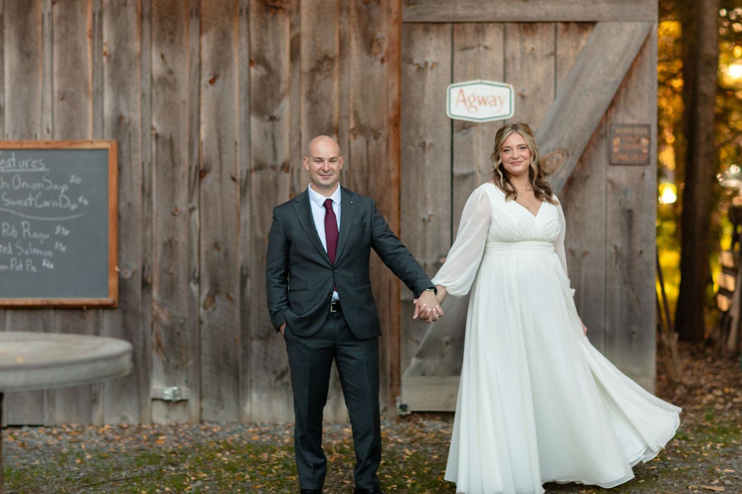 Wedding couple poses in front of rustic wooden barn during golden hour.