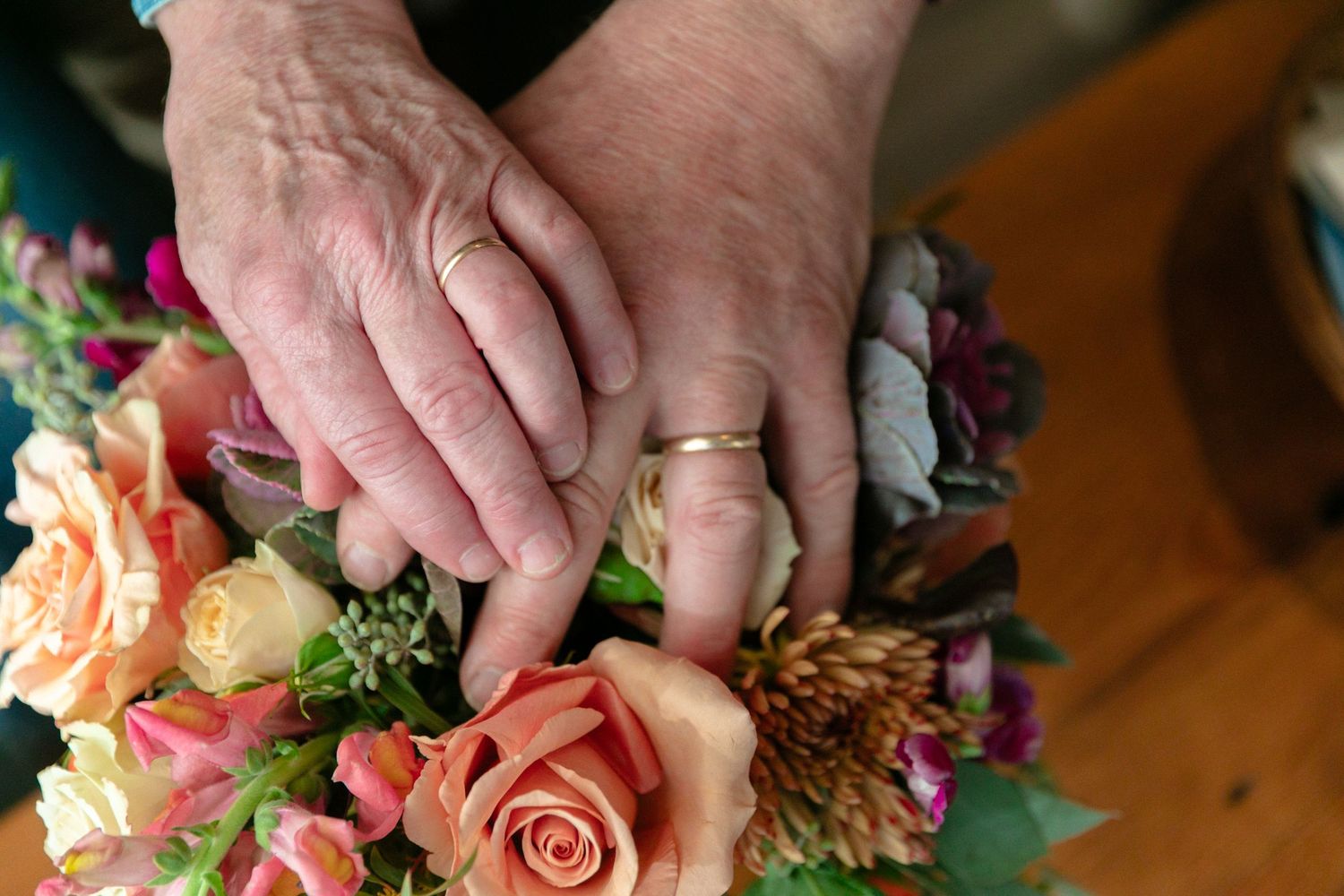 Close-up of hands arranging peach and pink roses in a floral arrangement.