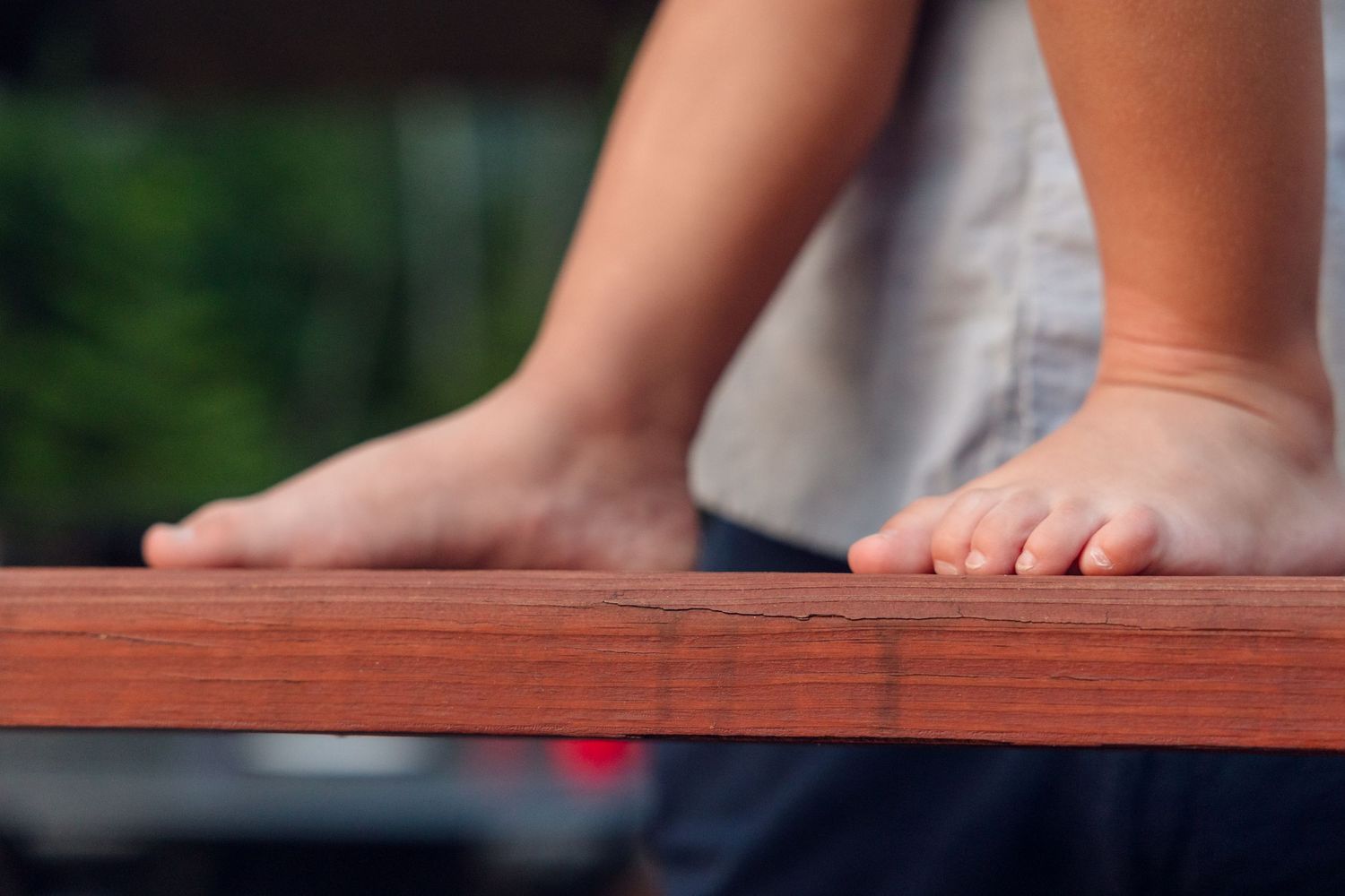 Close-up of bare feet resting on a wooden dock or railing near water.