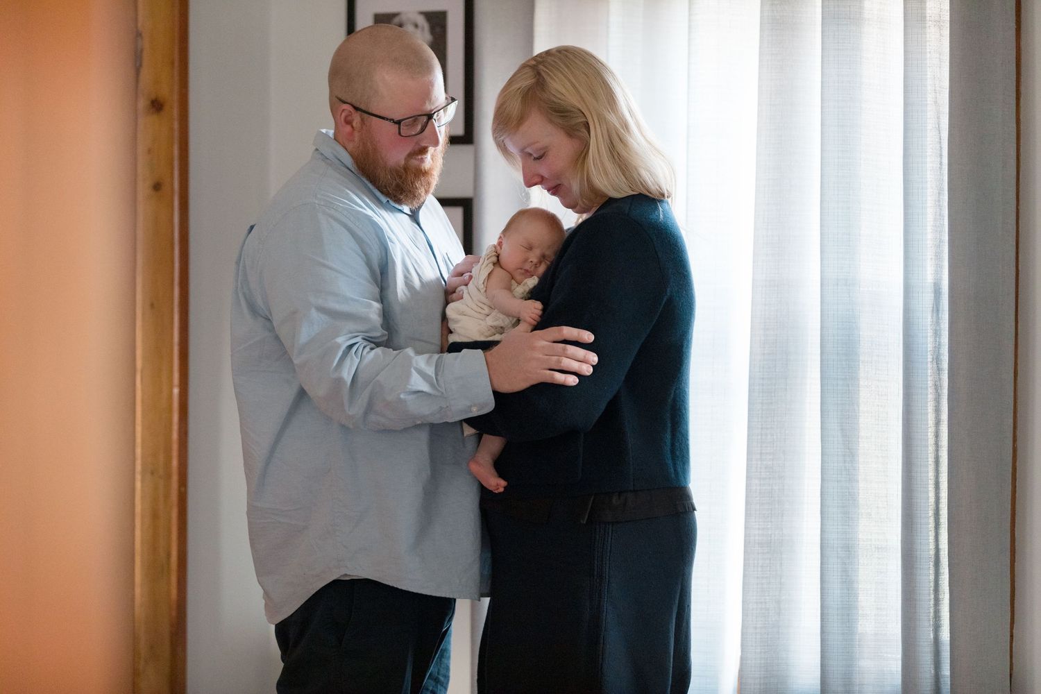Parents tenderly holding their newborn baby near a window.
