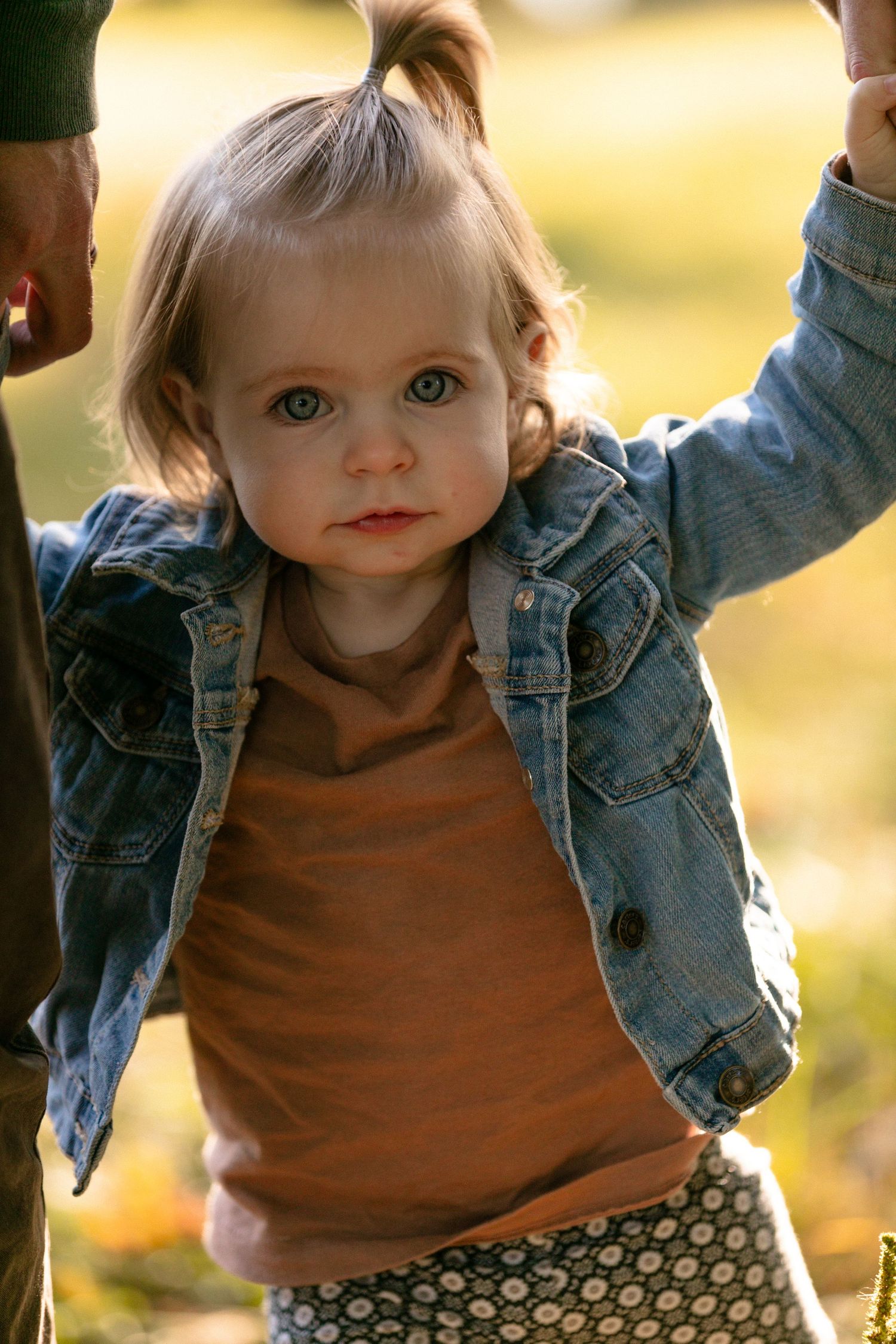 Toddler in denim jacket and brown shirt smiling during outdoor autumn photoshoot.