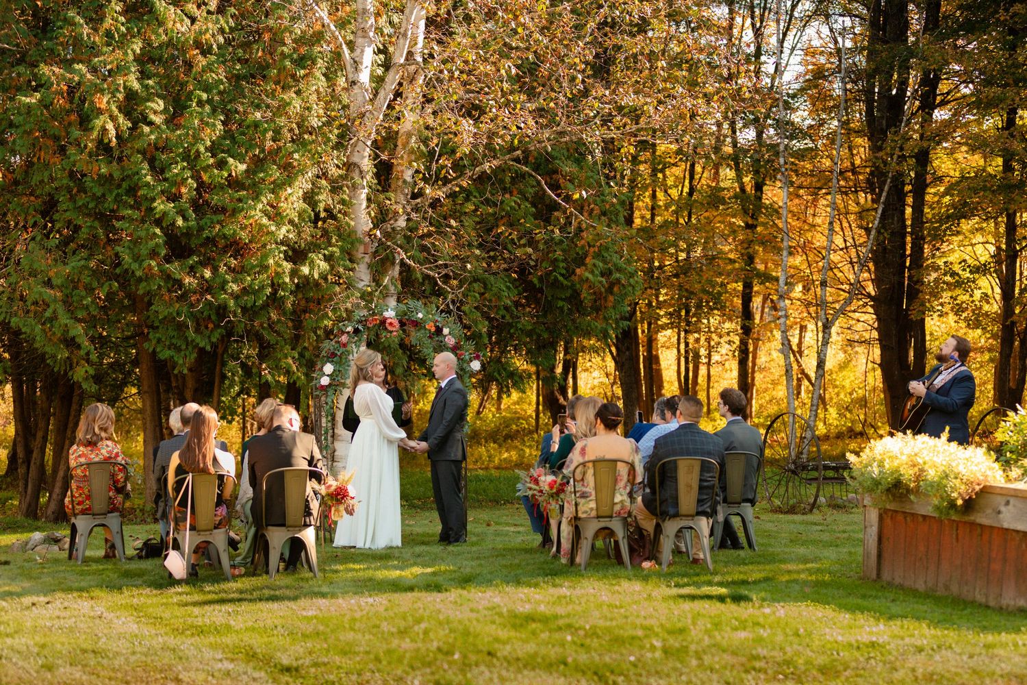 Wedding party gathering outdoors during golden hour among autumn trees.