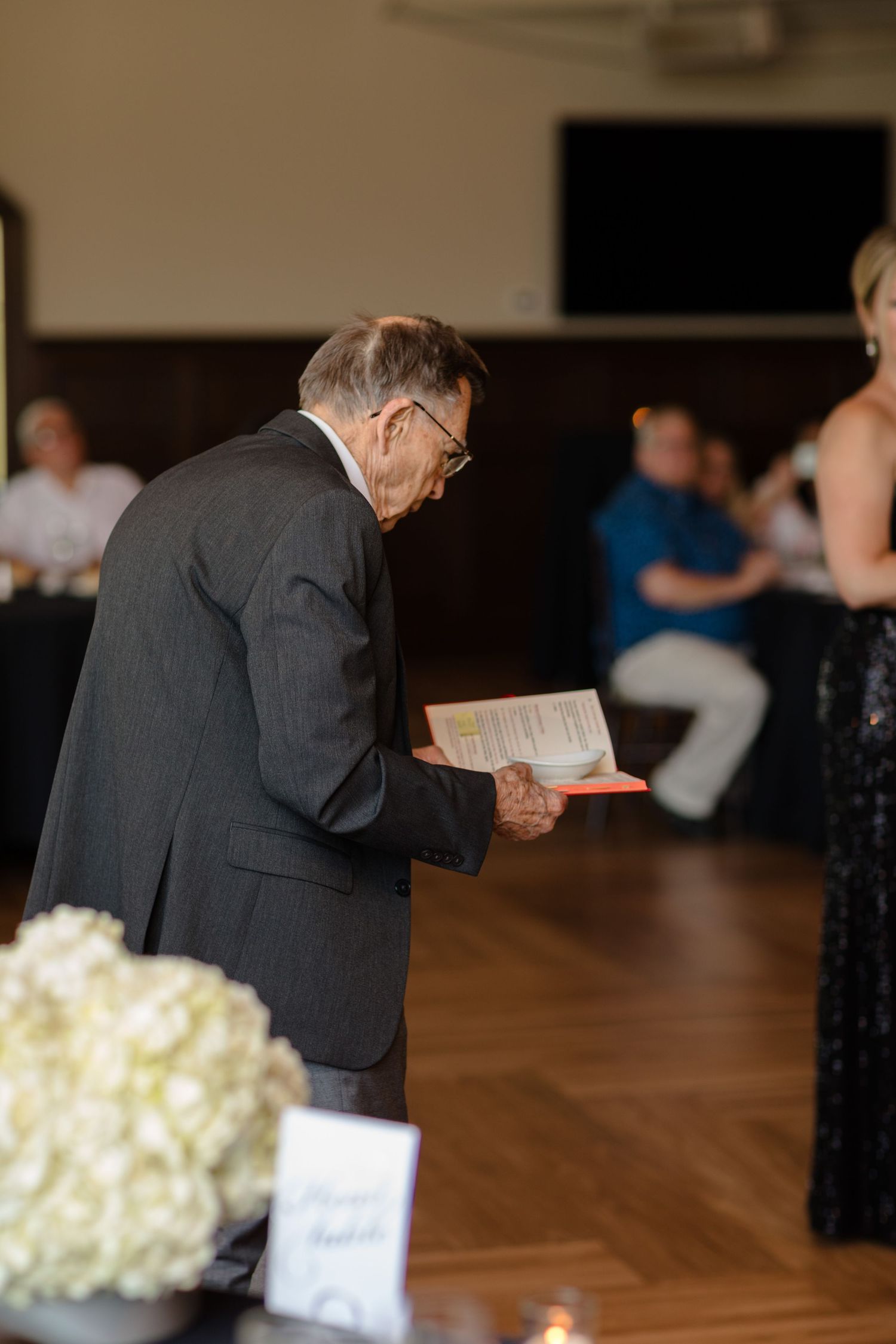 People holding up phones to capture memories at a formal gathering with white floral centerpieces.