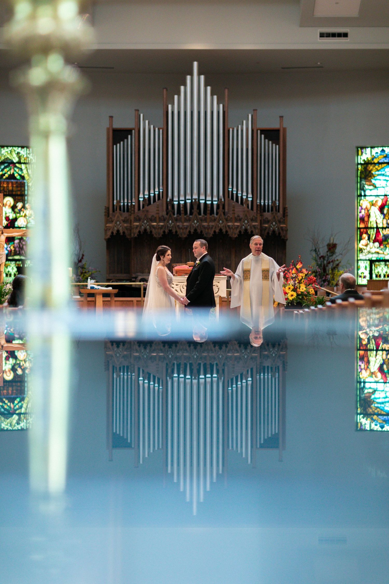 A wedding ceremony in a church with a grand pipe organ and stained glass windows reflected in artistic composition.
