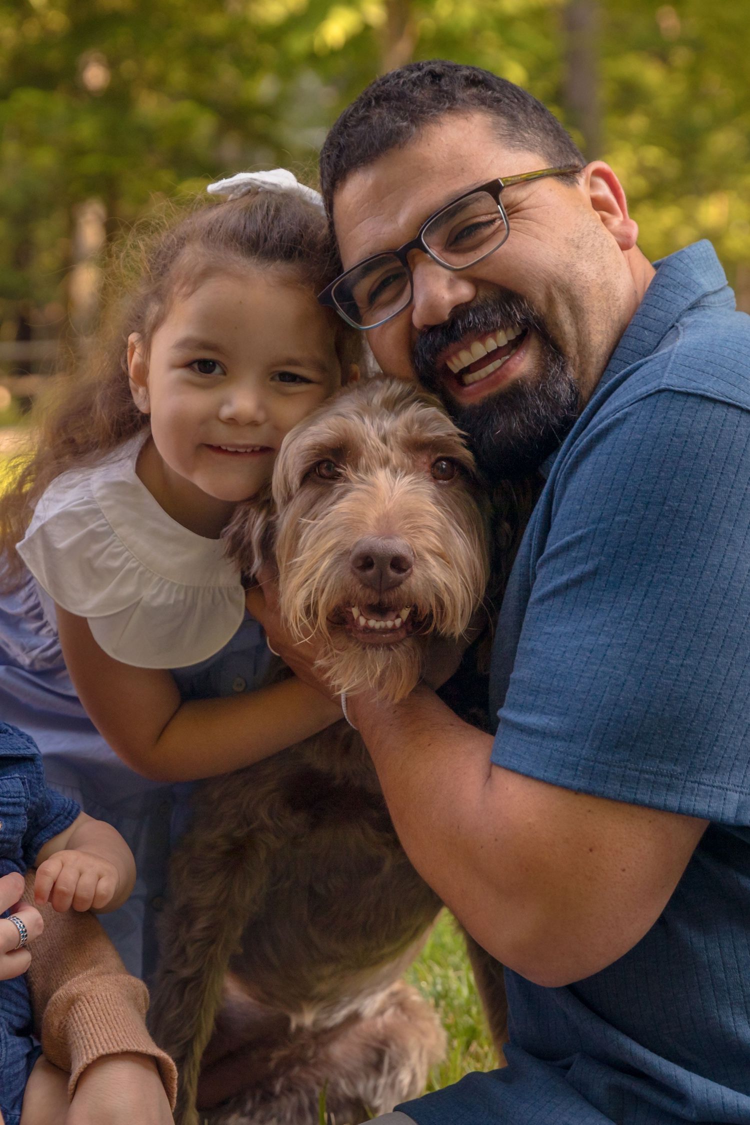 A happy family poses outdoors with their scruffy brown dog on a sunny autumn day.