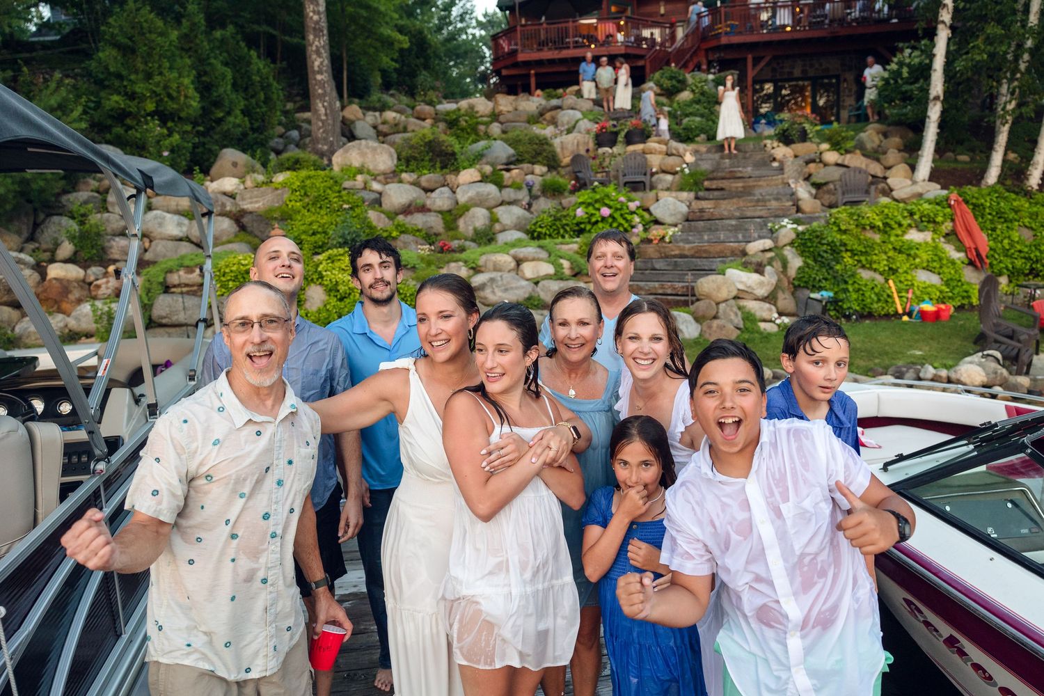 Large group photo of celebration attendees outdoors near a lakeside deck.