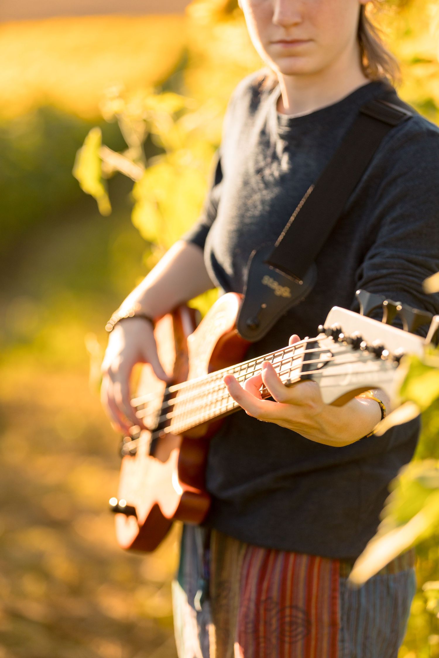 Close-up of hands playing bass guitar against sunlit background.