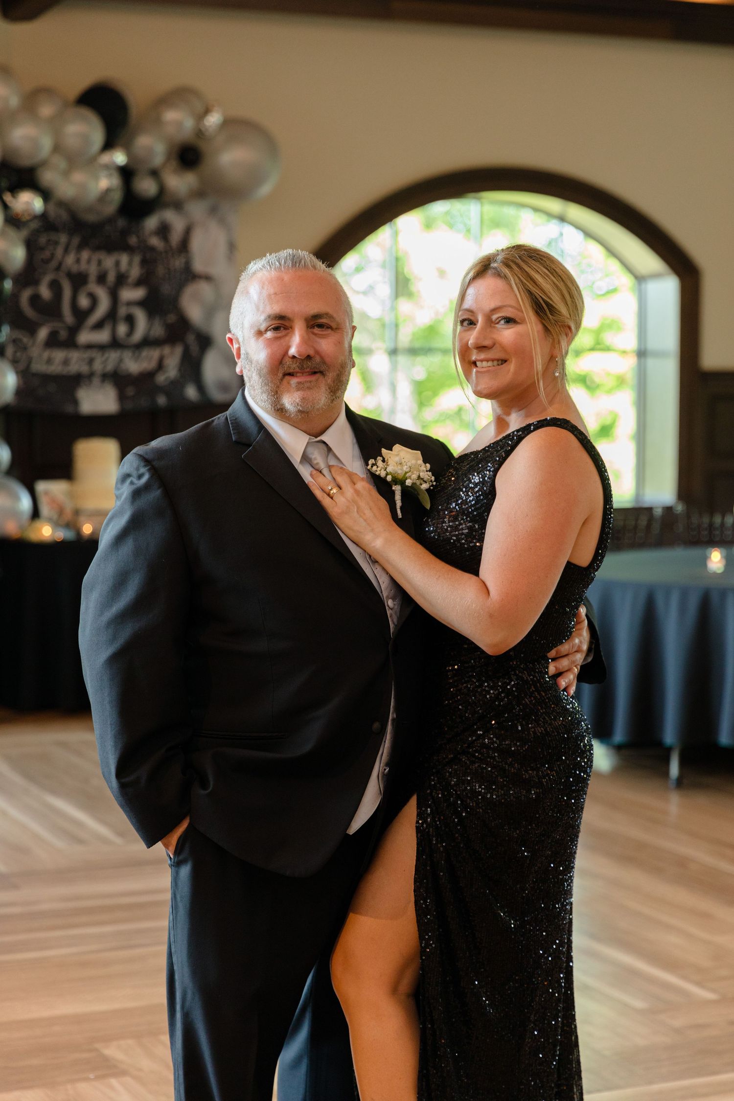 A couple dances together in formal attire at an event with silver balloon decorations.