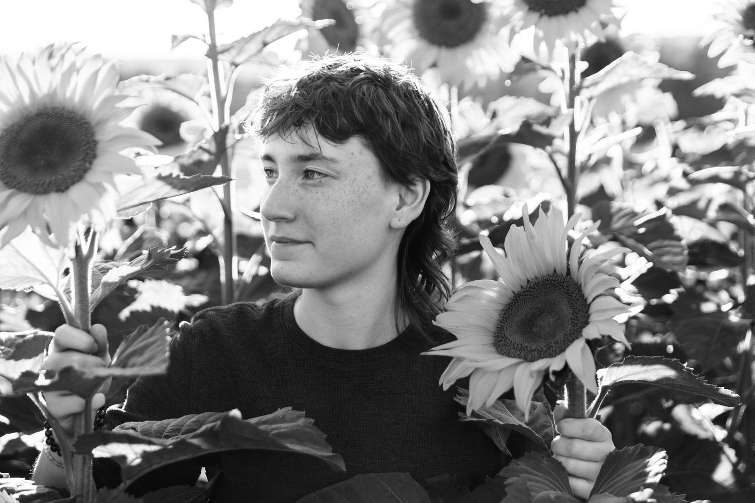 Black and white portrait amidst towering sunflowers in a garden setting.