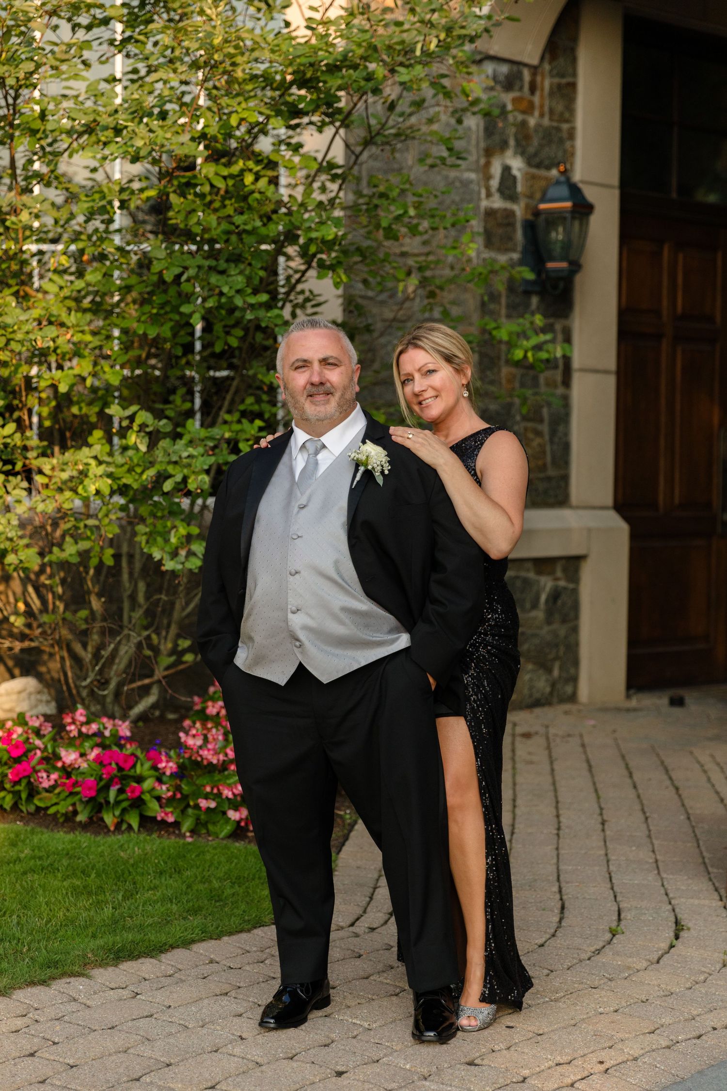A couple posing outdoors on a stone patio with blooming flowers and greenery.