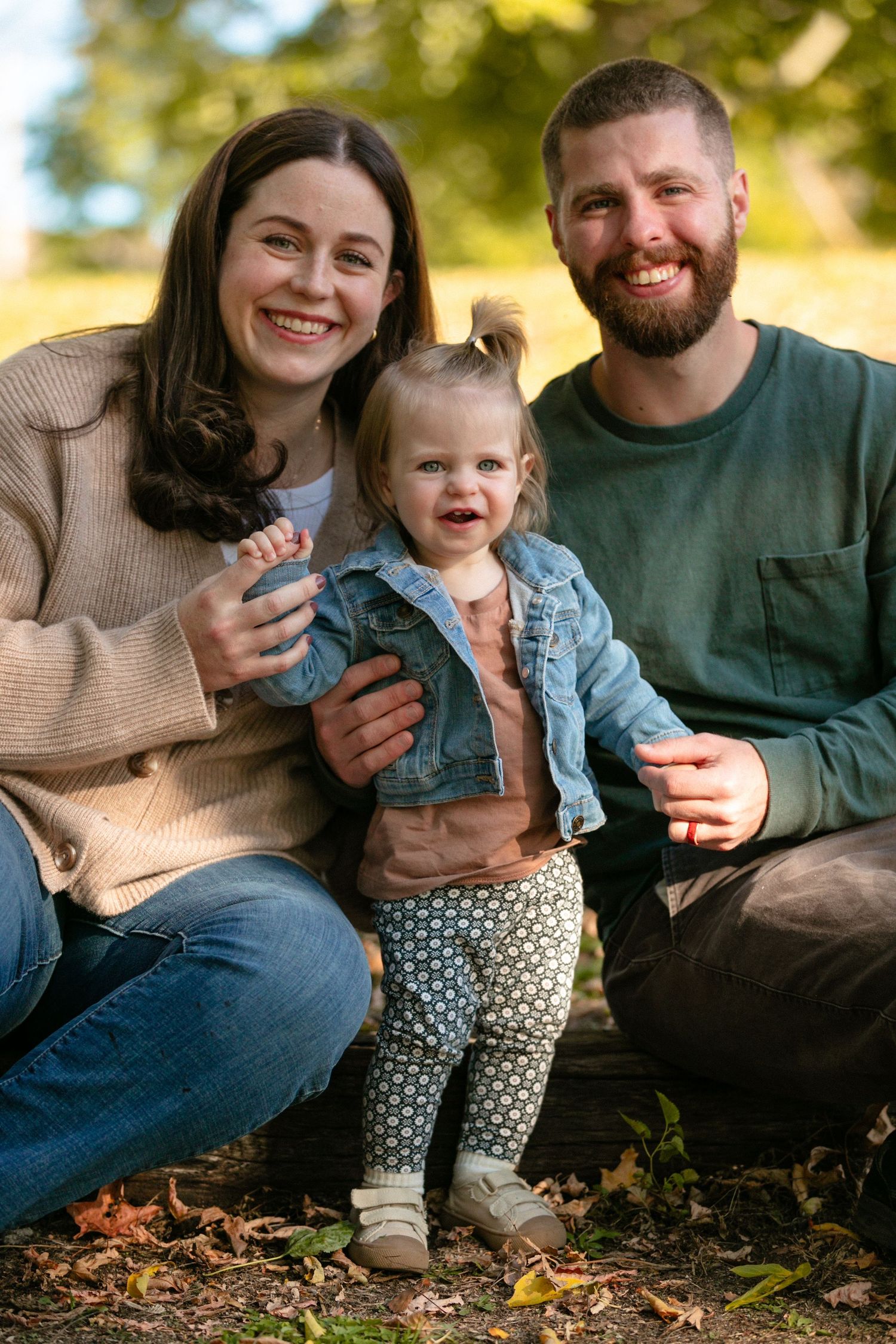 Family of three sitting together on ground during autumn photoshoot.