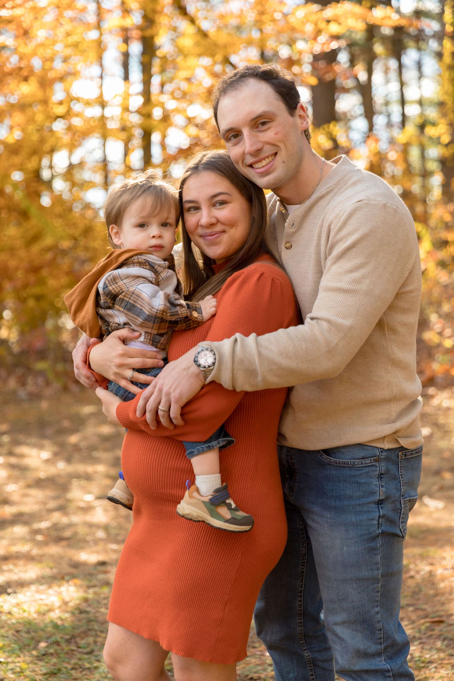 Happy family embracing in autumn forest setting with orange and golden leaves.