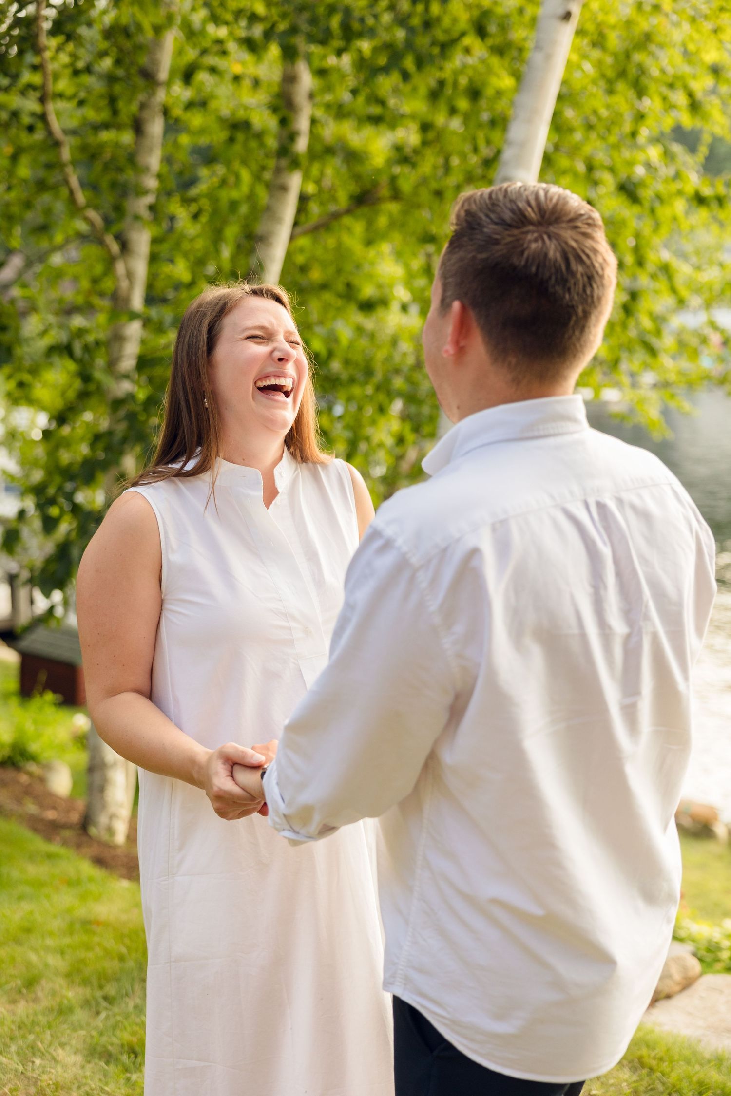 Joyful interaction between two people wearing white during a sunny outdoor photo session.