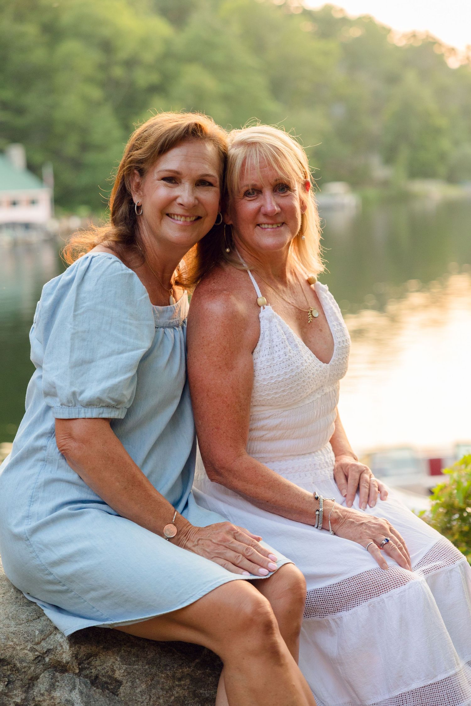 Two people in light summer clothing sit together by a serene lakeside during golden hour.