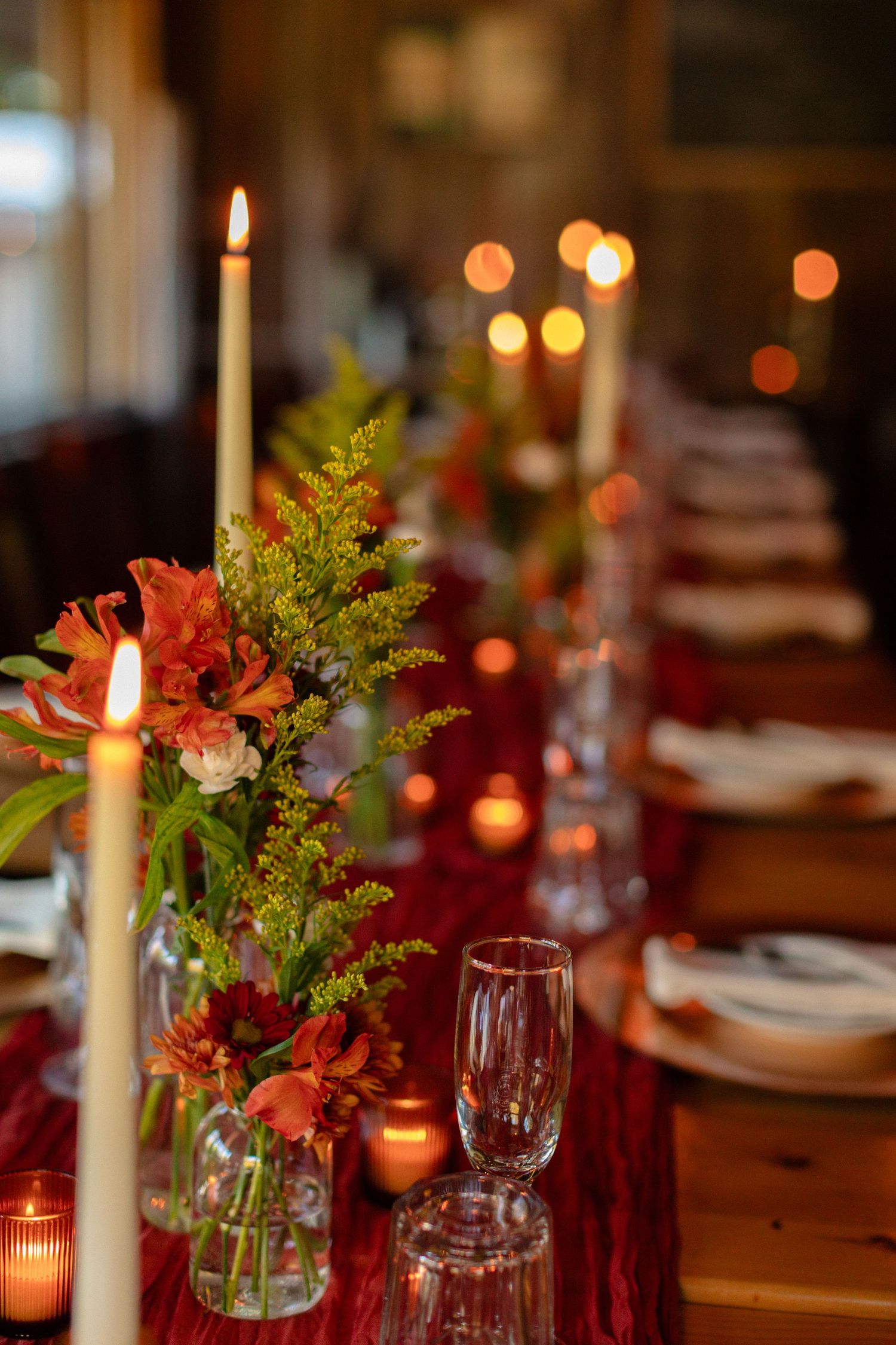 Elegant wedding reception table with candles and burgundy floral centerpieces.