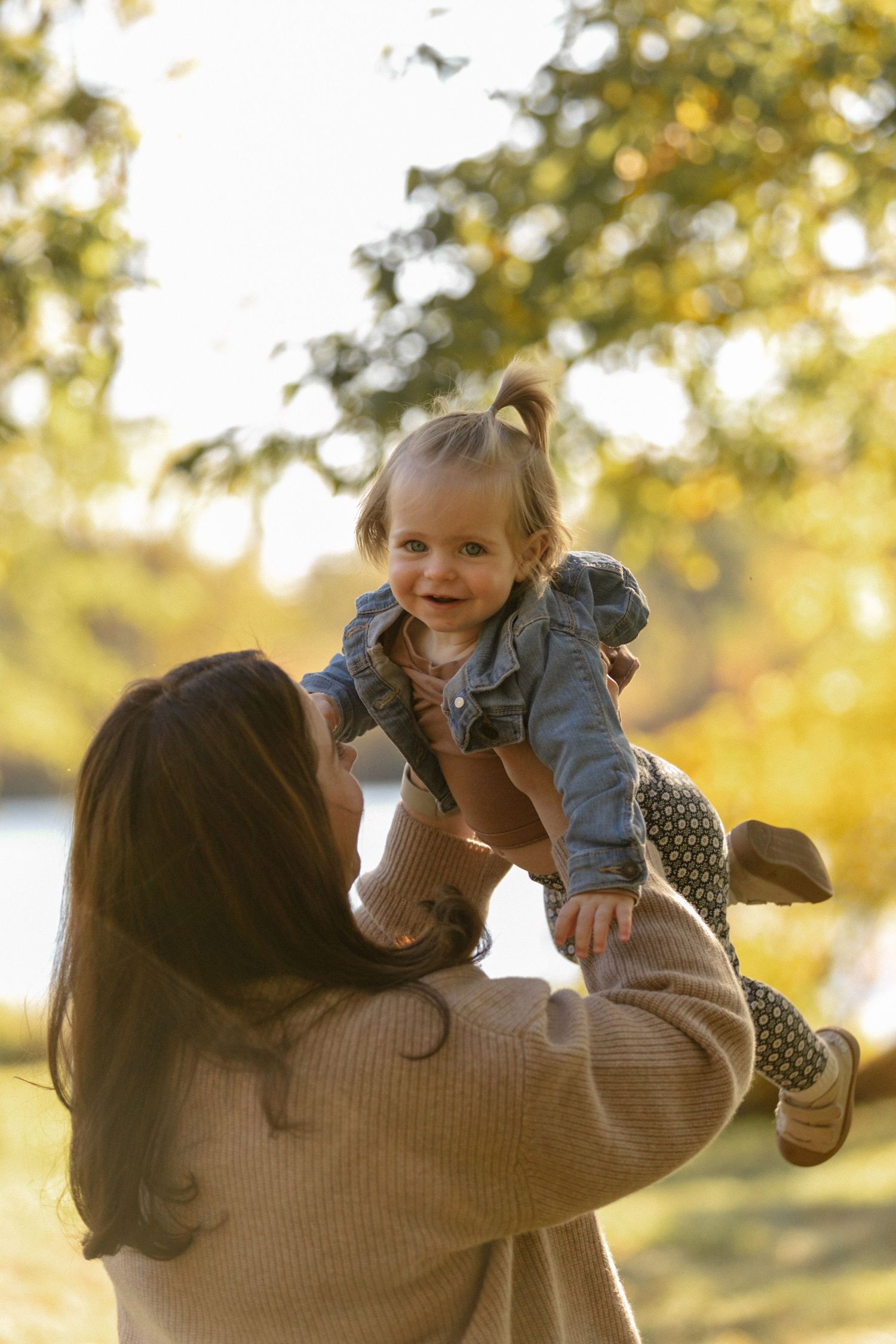 Parent lifting child playfully in air during autumn outdoor photoshoot.