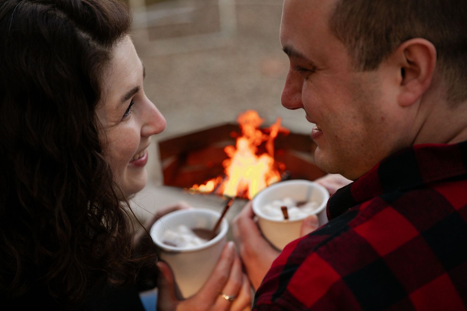 Intimate moment shared between couple near glowing fire pit at night.
