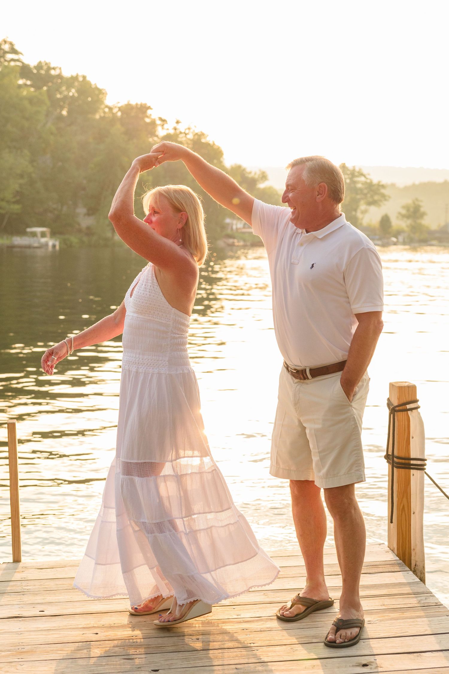 A couple dances together on a wooden dock at sunset with a lake in the background.