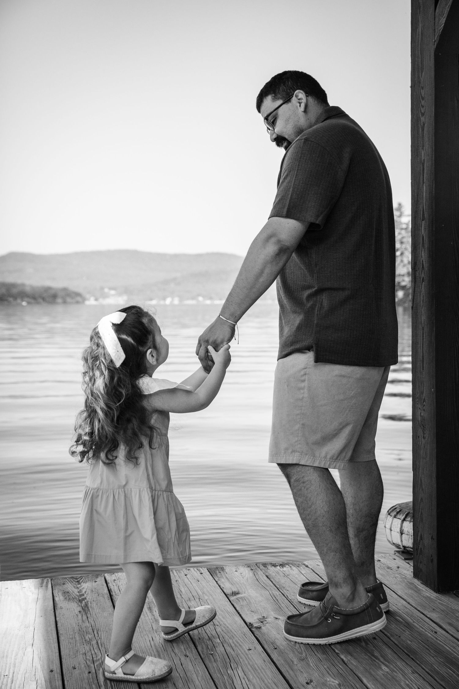A tender moment shared between parent and child holding hands on a lakeside dock.