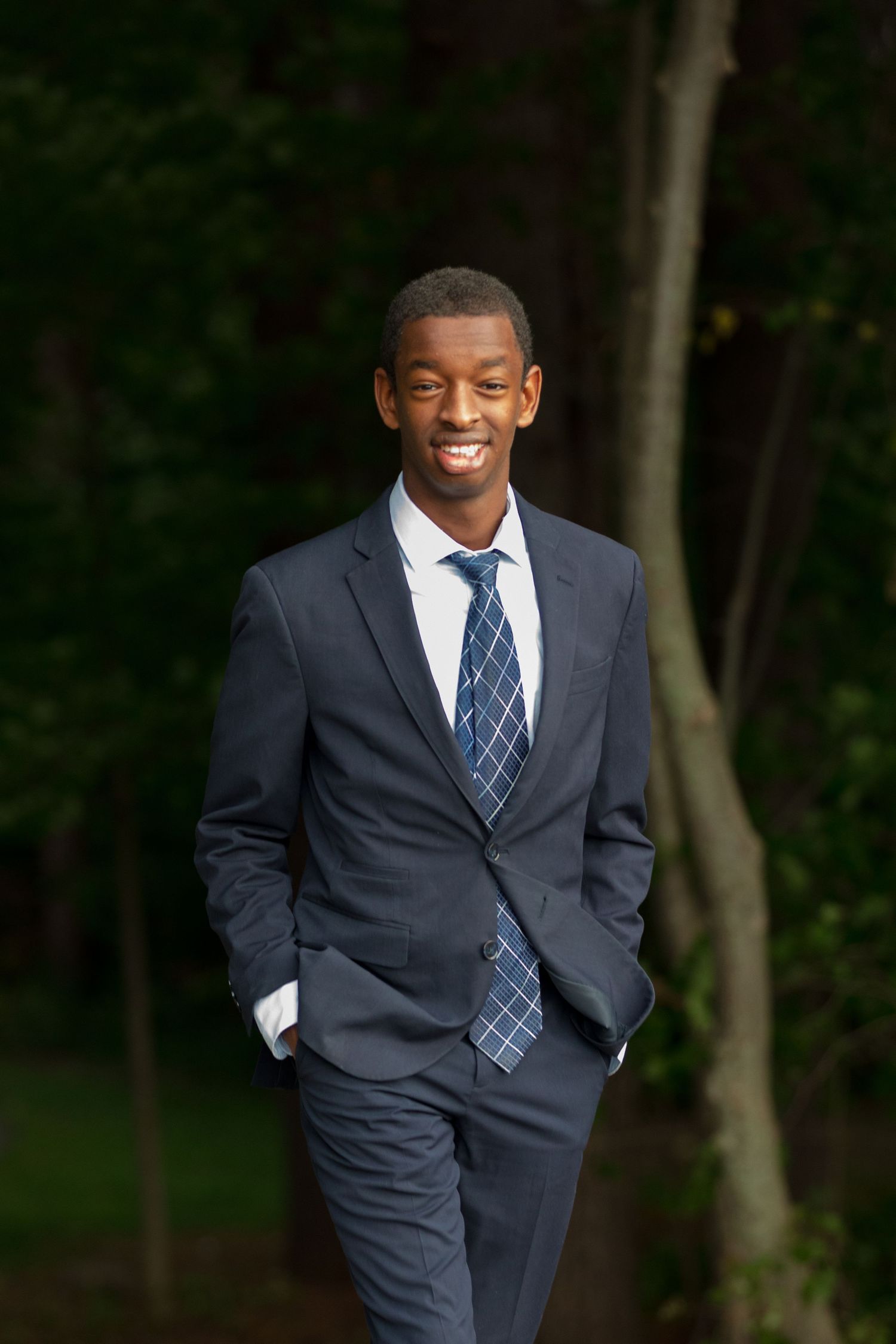 A person in a navy suit and striped tie poses outdoors for professional photos.