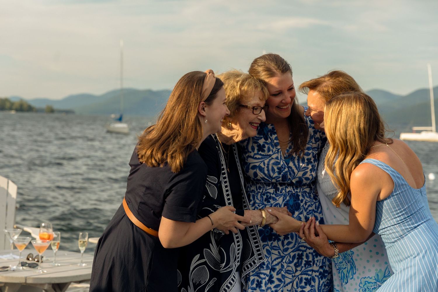 Group of friends enjoying drinks and conversation on a boat deck with mountains visible in the background.