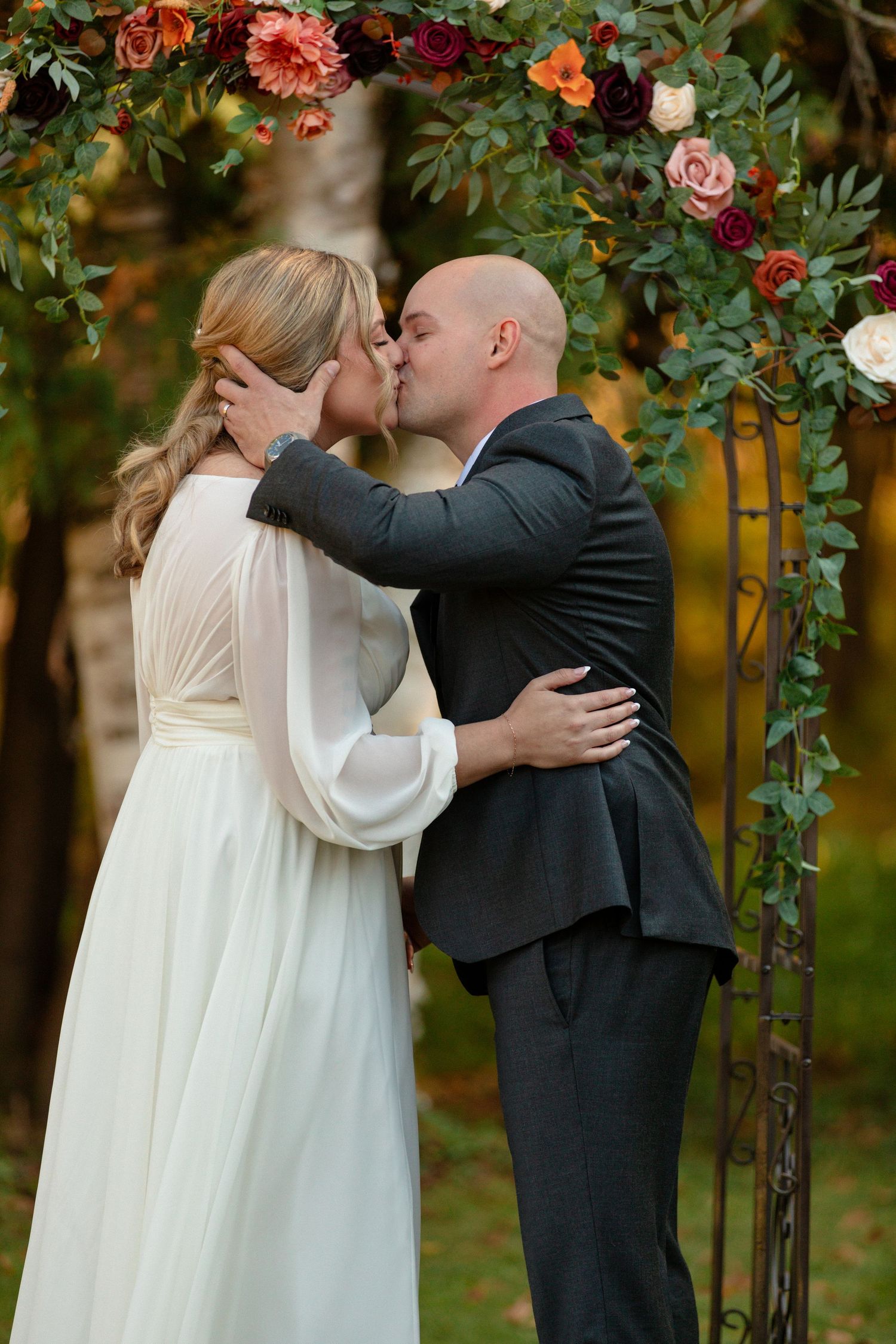 Romantic wedding ceremony under a floral arch in autumn garden.