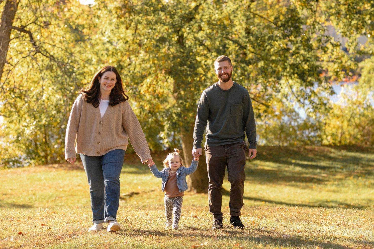 Family walking together through a park with golden autumn trees in background.