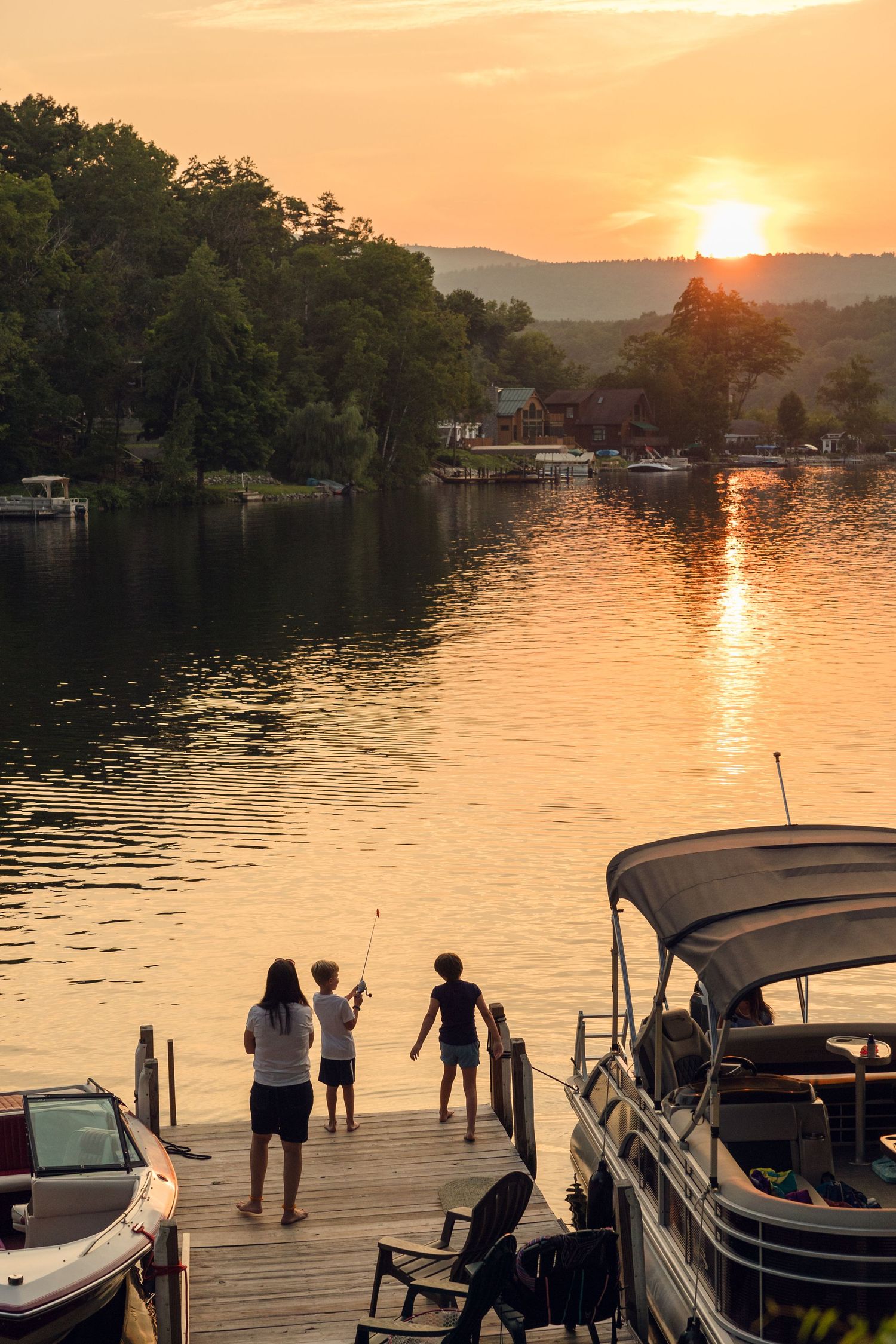 A beautiful sunset over a lake with boats docked at a wooden pier.