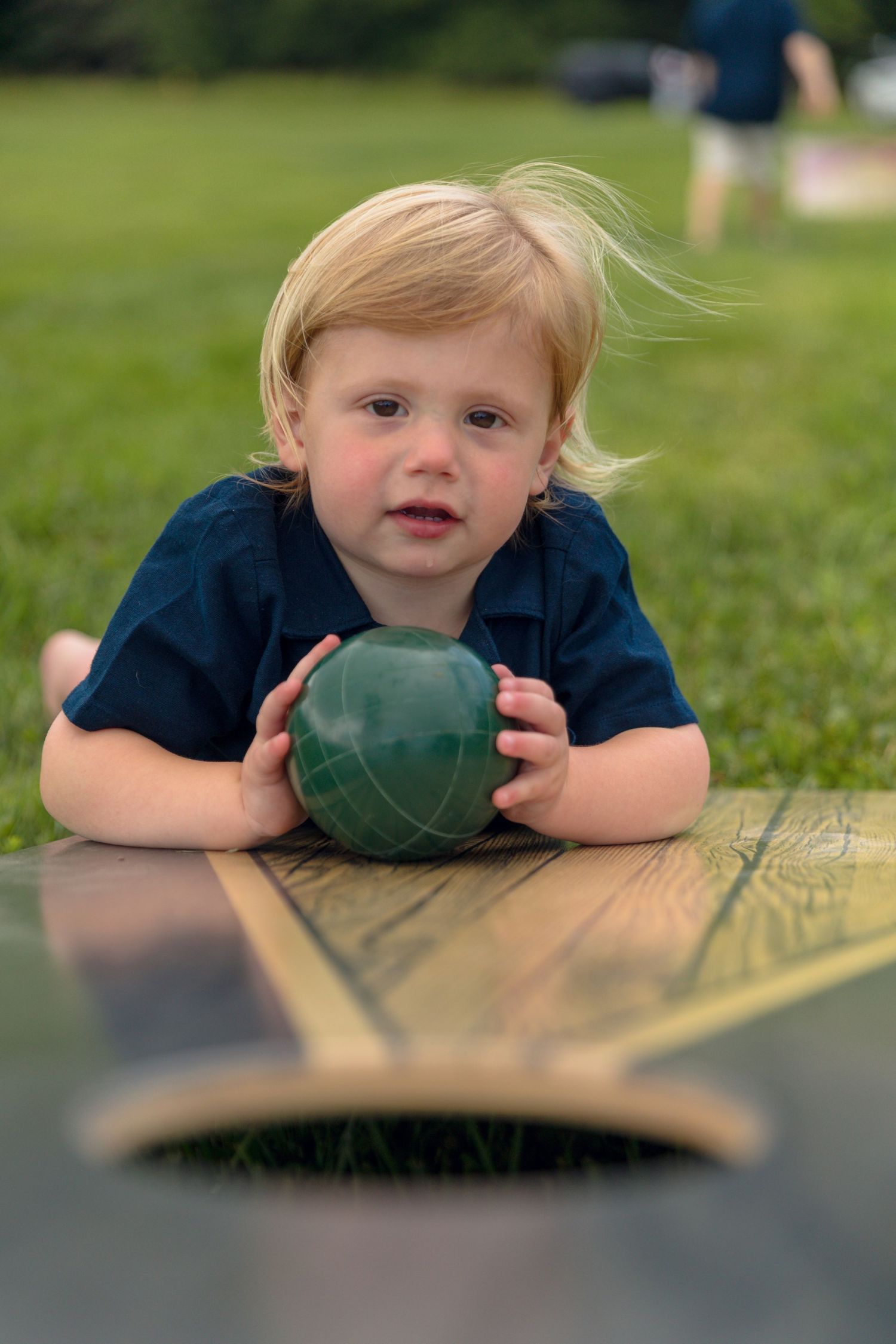 Child lying on wooden surface outdoors with playful expression.