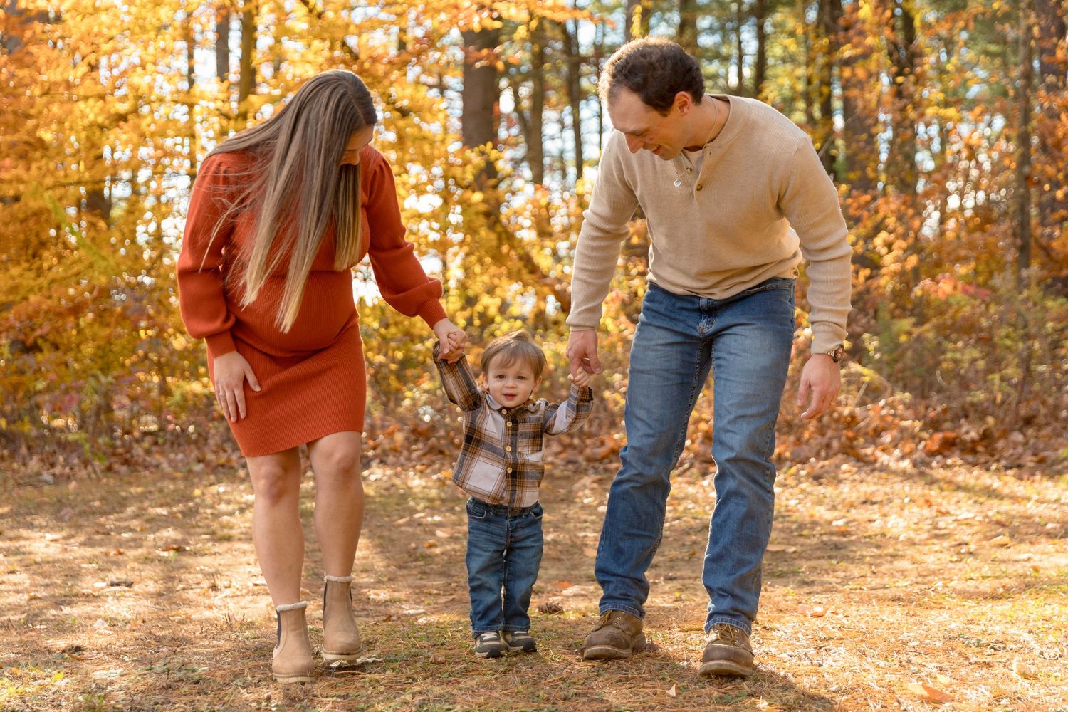 A family's feet and legs are shown against fallen autumn leaves in a wooded setting.