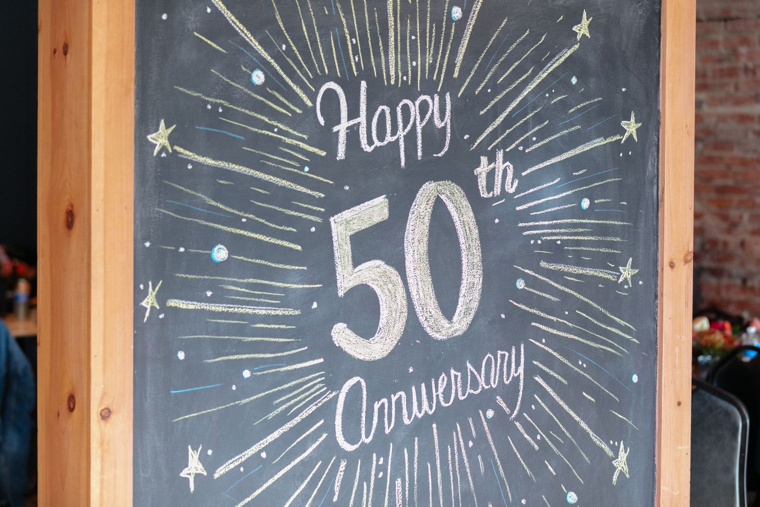 Chalkboard sign with decorative lettering displaying 'Happy Anniversary' with starburst design.