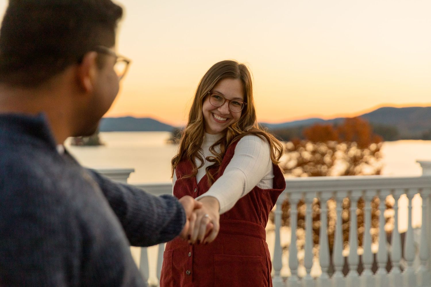 Couple shares romantic moment at sunset with ocean and mountains in background.