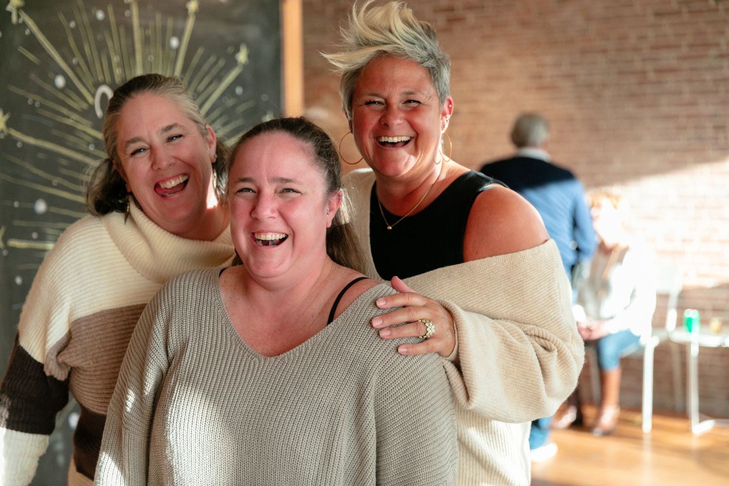 Three people sharing a joyful laugh together against a brick wall background.