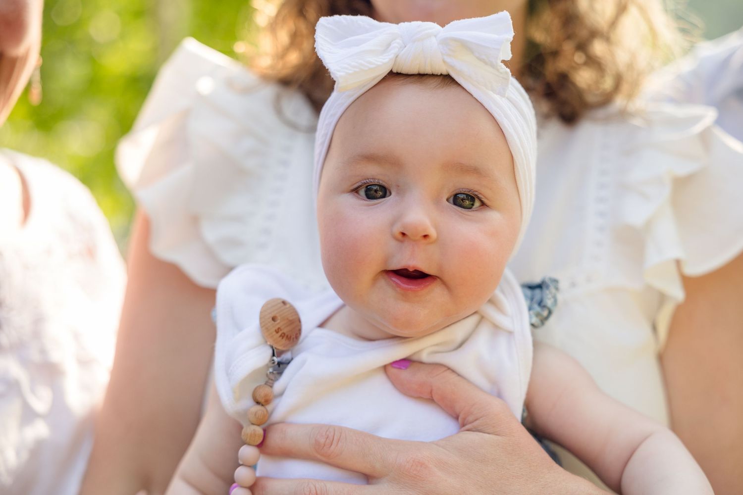 Close-up shots of a baby wearing a white bow headband and dress in natural lighting.