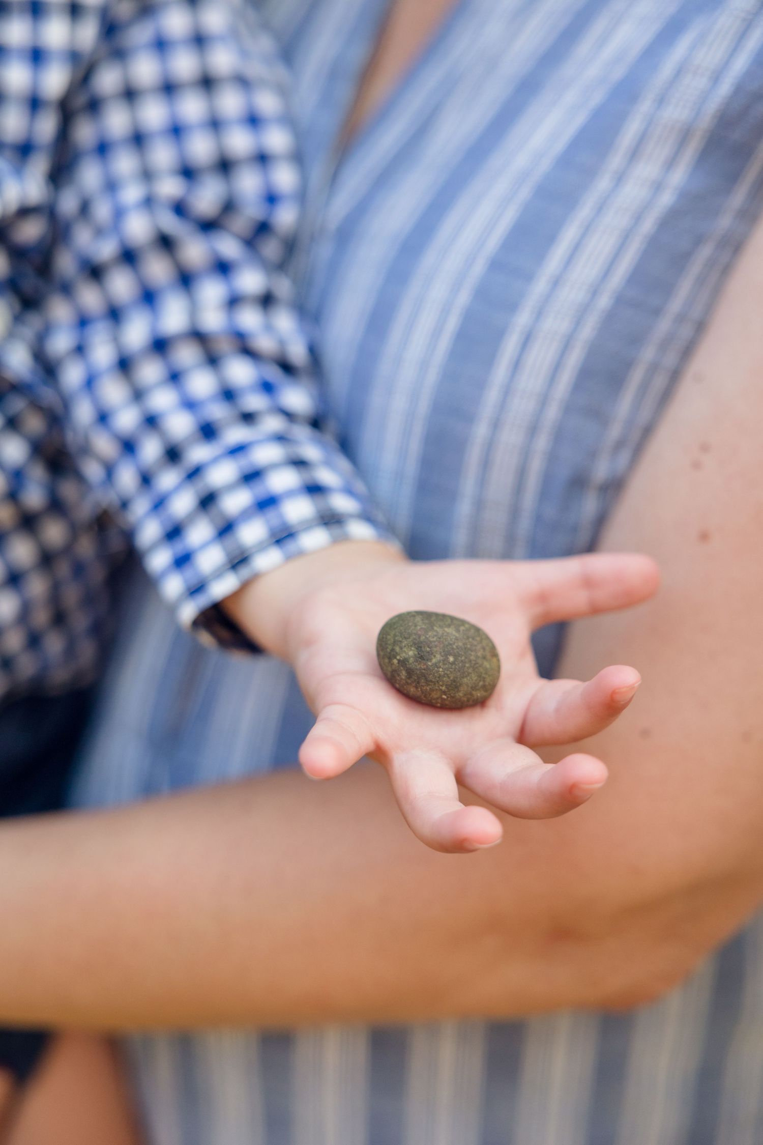 Close-up of hands holding a smooth gray stone against blue striped fabric.