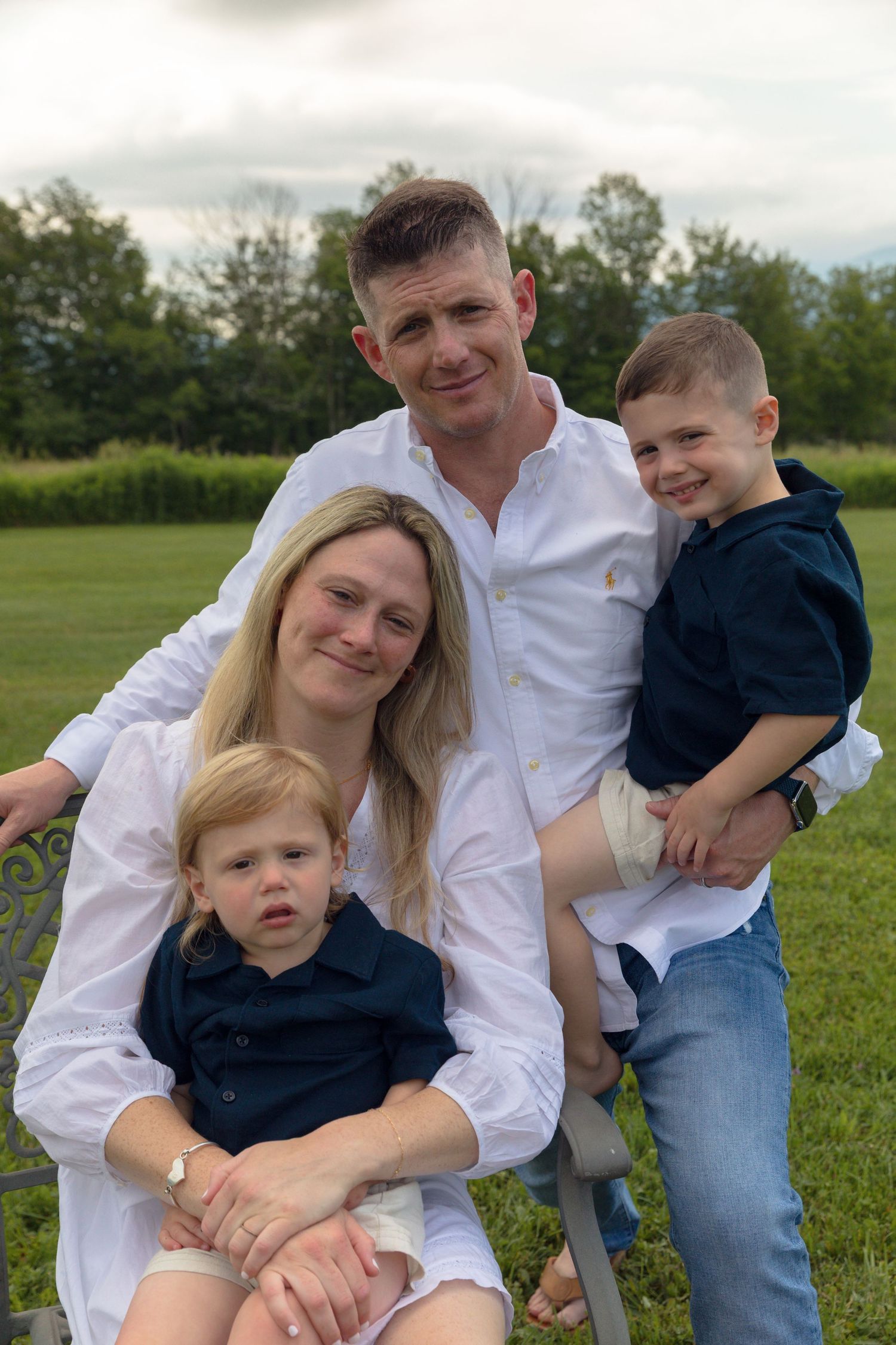 Family of four posing together on grass for a casual outdoor photo.