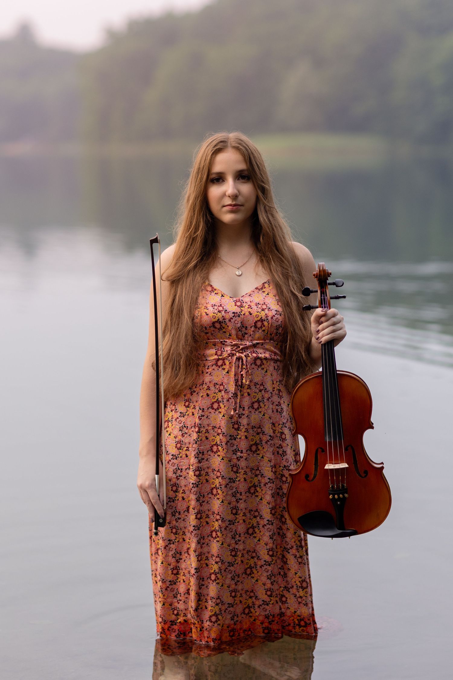 A floral dress and violin create an artistic composition by the tranquil lake.
