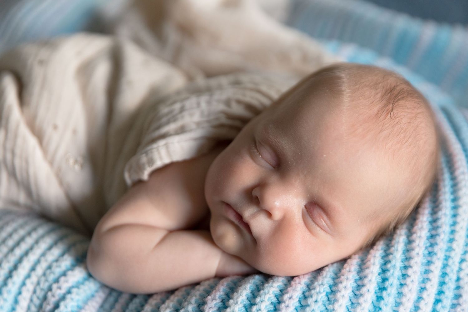 Peaceful sleeping baby on blue and white striped blanket.
