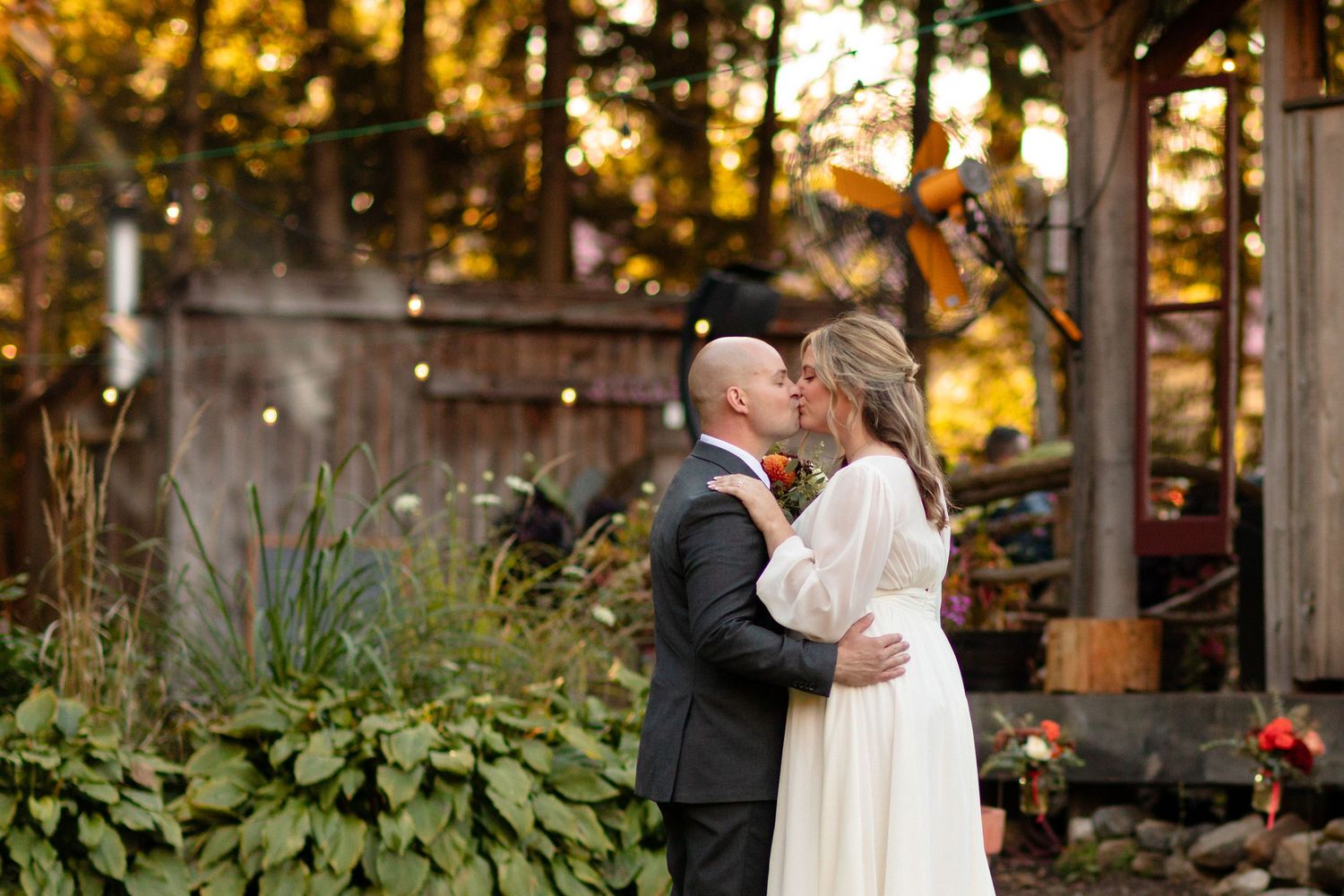 Romantic wedding couple embraces during outdoor autumn ceremony under wooden pergola.