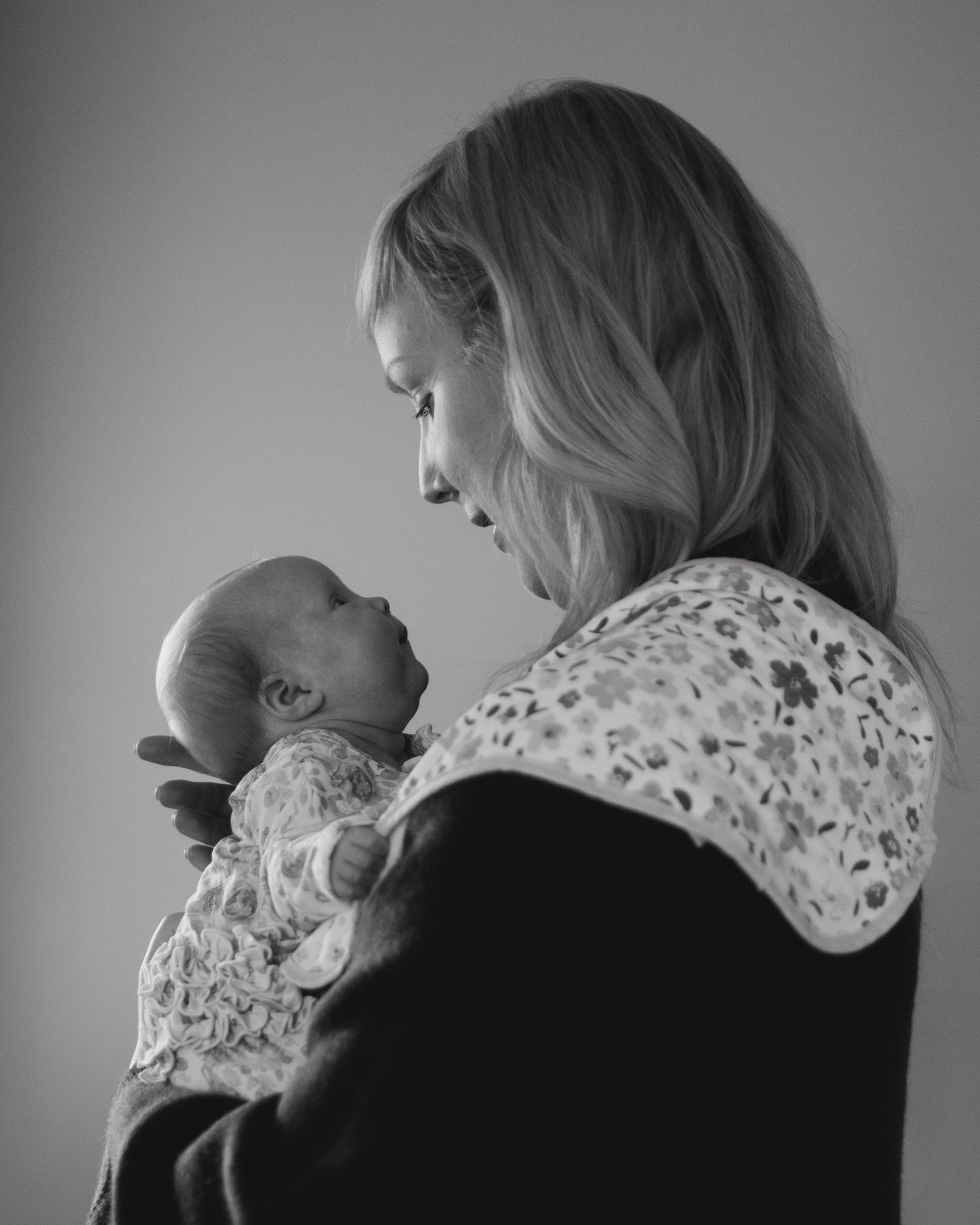Black and white portrait of parent holding newborn against grey background.