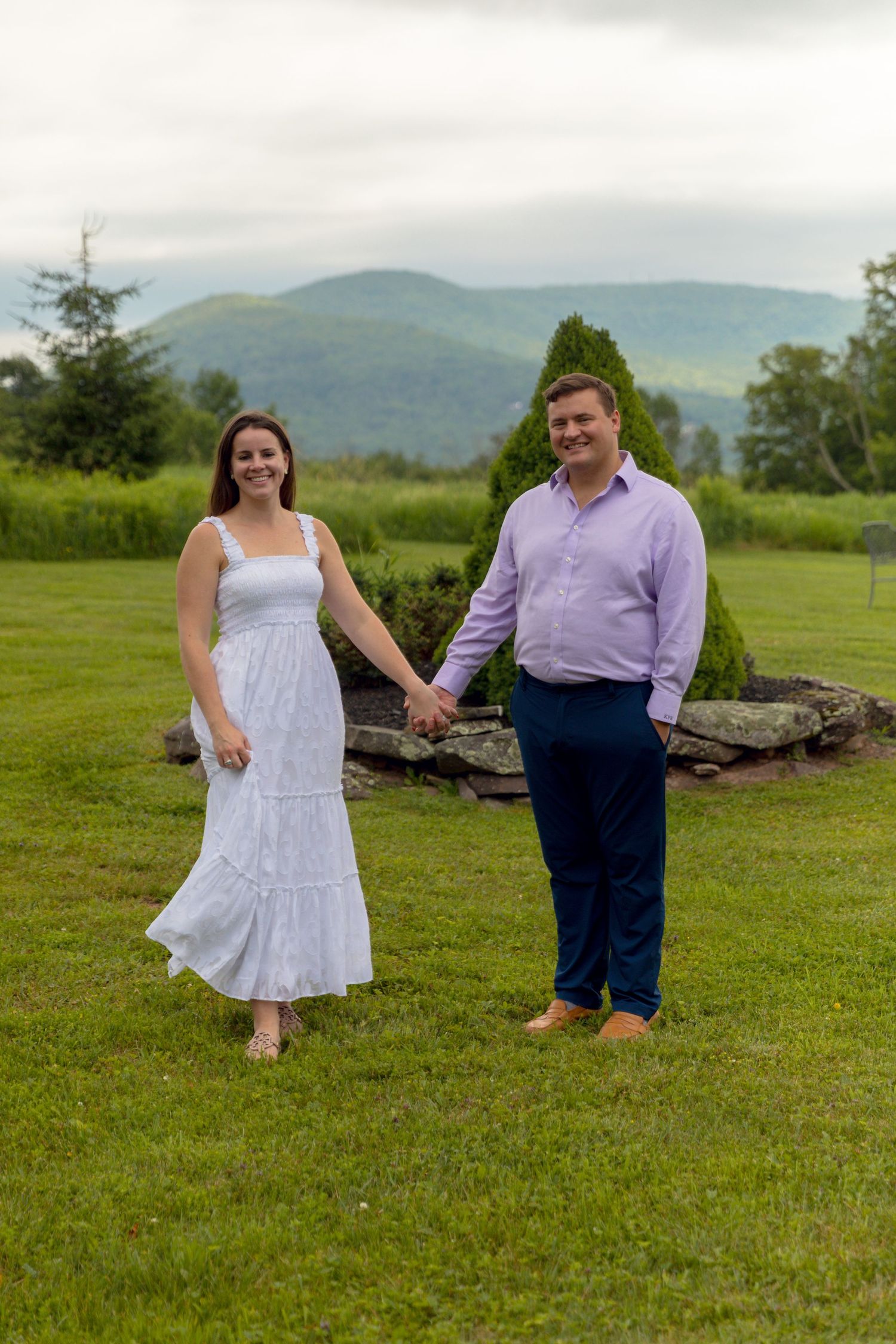 A couple poses together on a grassy hillside with mountains in the background, creating a romantic outdoor scene.